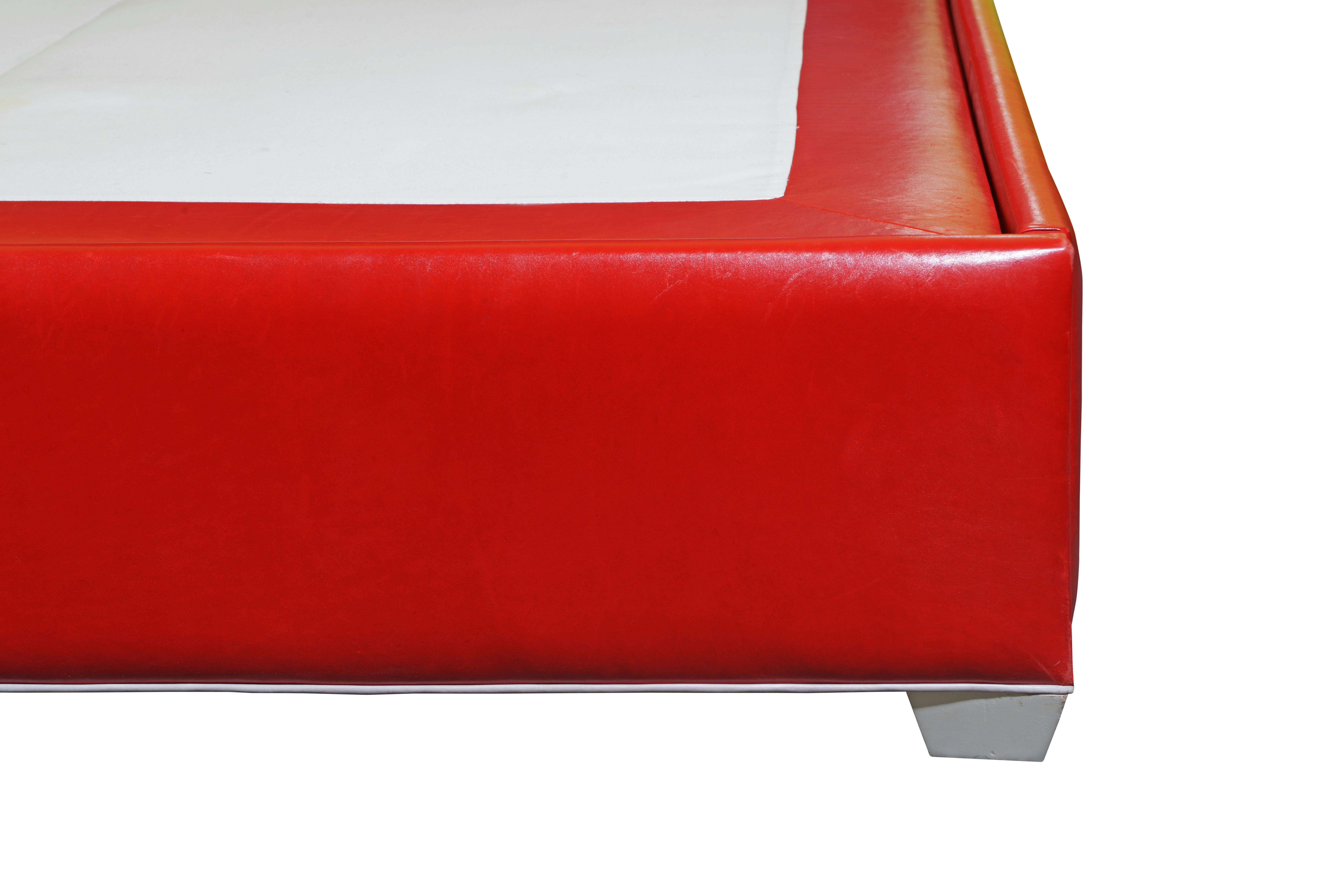 Lipstick-red leather bed featuring a Moorish-inspired arch headboard adorned with contrasting white leather piping and buttons. The bed boasts a fully upholstered red leather platform, supported by low, white-painted feet.