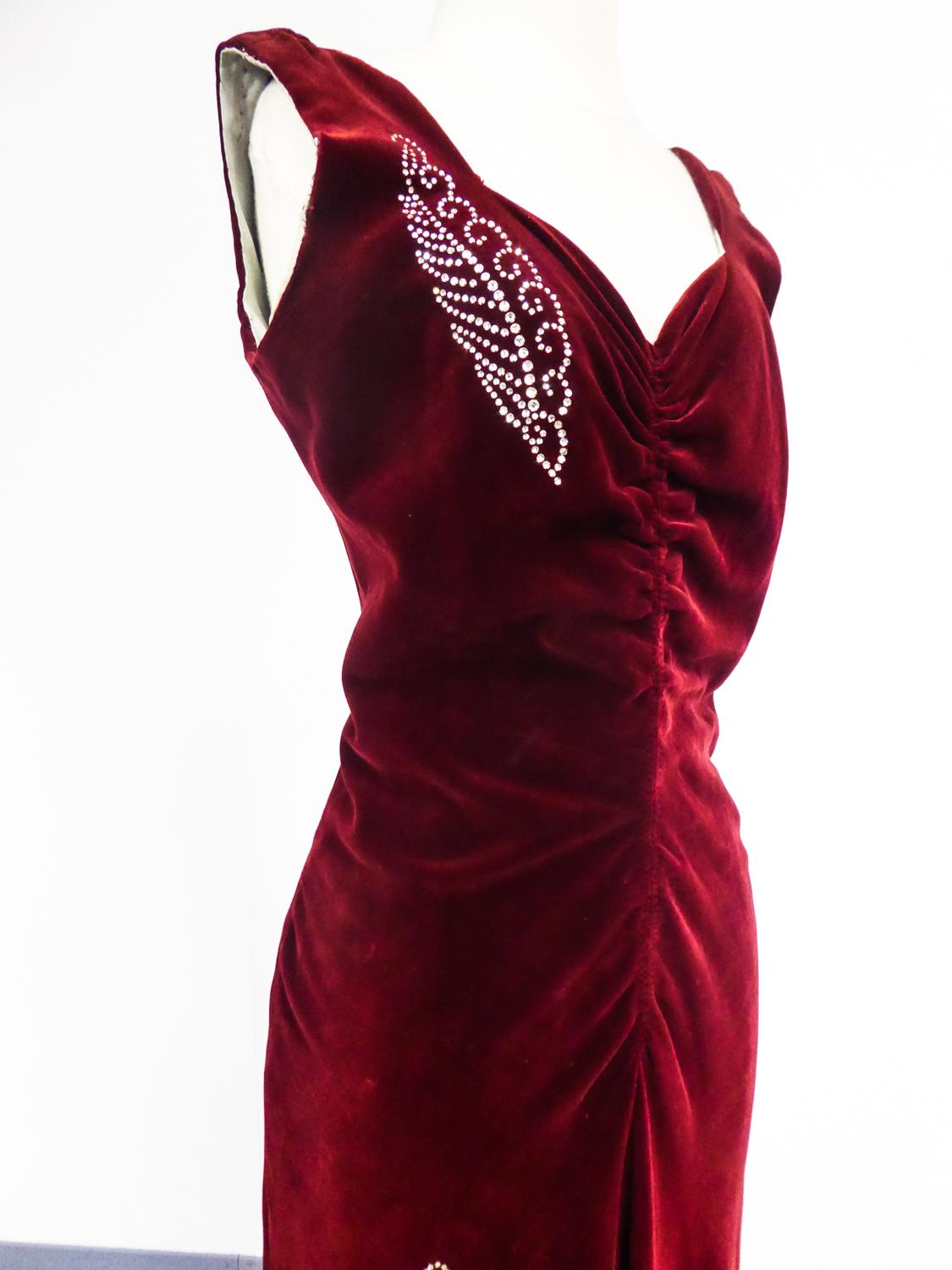 Circa 1935
France

Rare robe longue de soirée de collection, Haute Couture française par Nicole Groult, célèbre sœur de Paul Poiret et datant des années 1935. Robe sans manches en velours de soie rouge carmin soulignée d'une broderie de strass