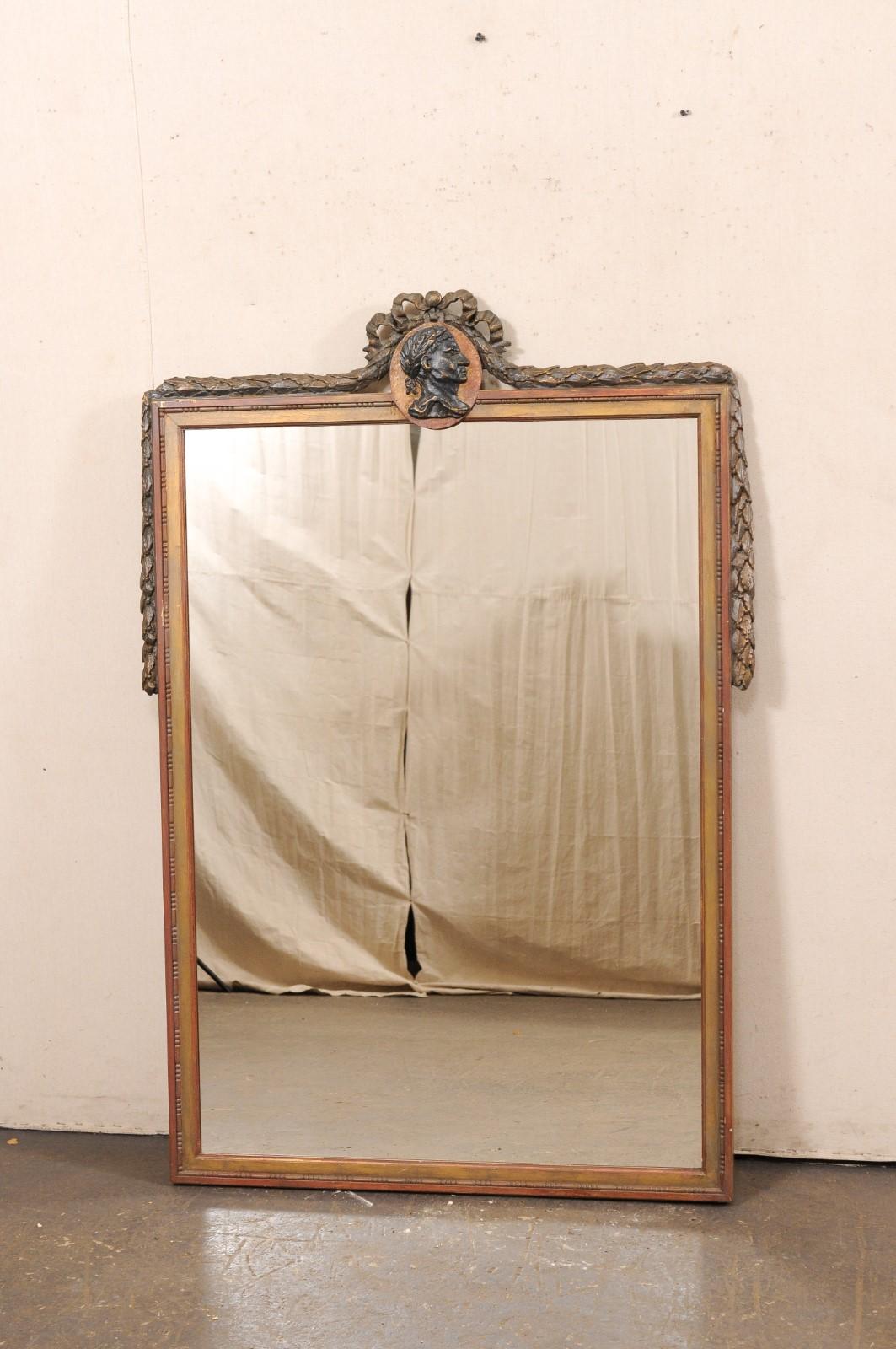 This vintage mirror, by American creator/manufacturer Niermann Weeks, has been designed in a Swedish Neoclassical style. The mirror features a profile bust of Caesar within the top crest center, adorned with carved bow and mirror shoulders draped in