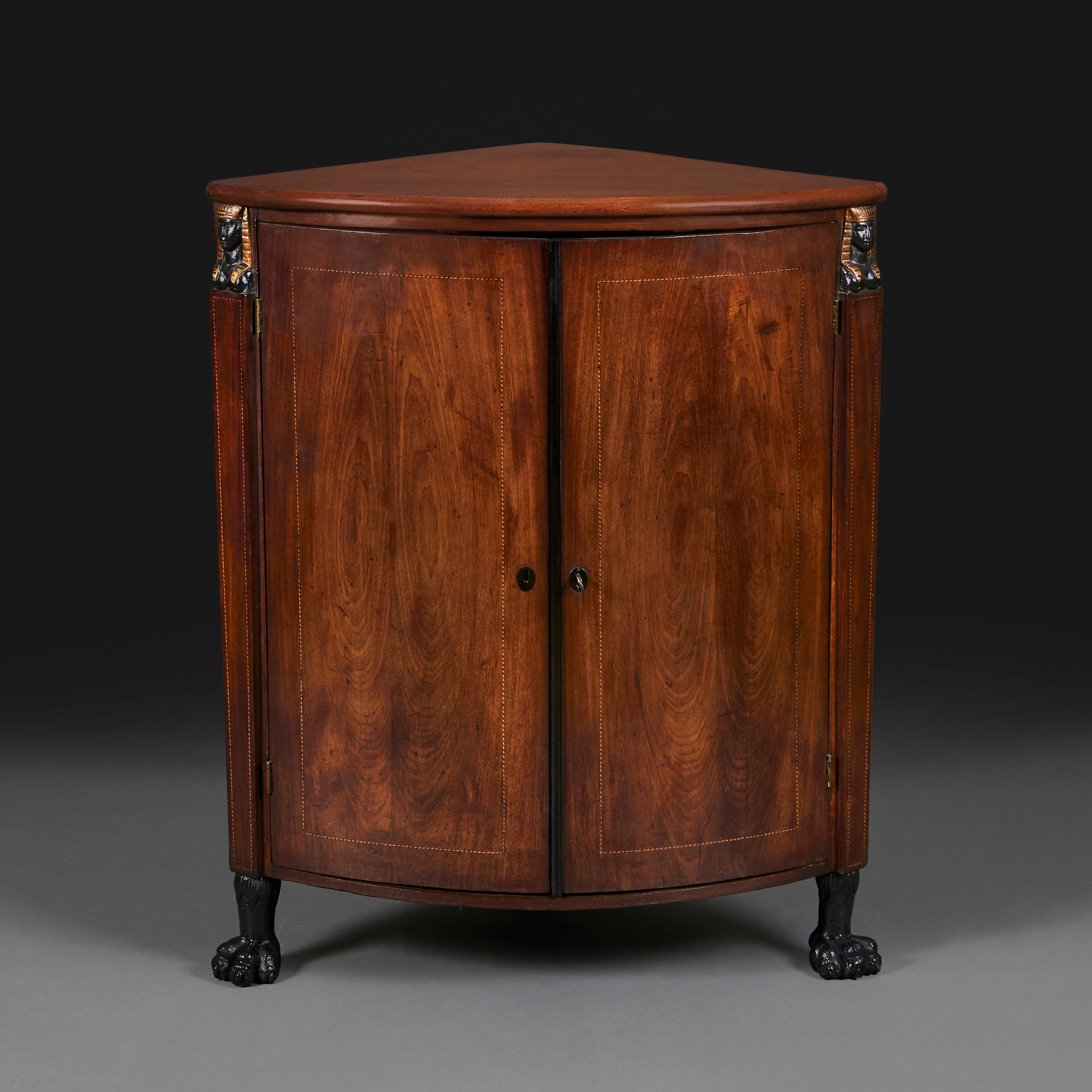 France, circa 1860

A mid nineteenth century mahogany corner cupboard, opening with two doors to the front, with inlaid marquetry beaded borders to the doors and the uprights, the uprights surmounted by Egyptian caryatids, and terminating in hairy