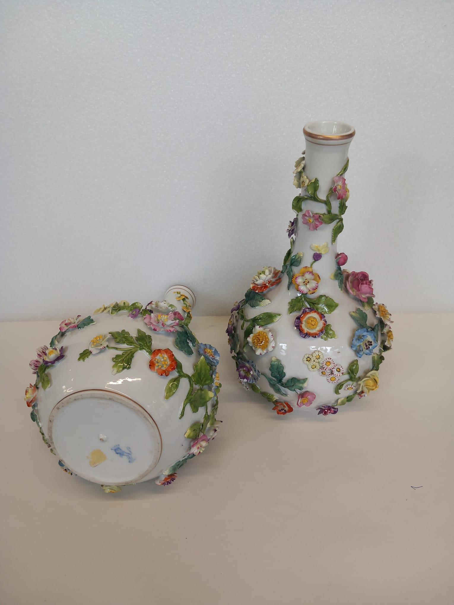 A nineteenth century pair of Dresden white porcelain vases, each encrusted with hand made ceramic flowers and leaves in the eighteenth century Meissen style.
The top edges of each case is decorated with a gold leaf painted edge, as is the bottom