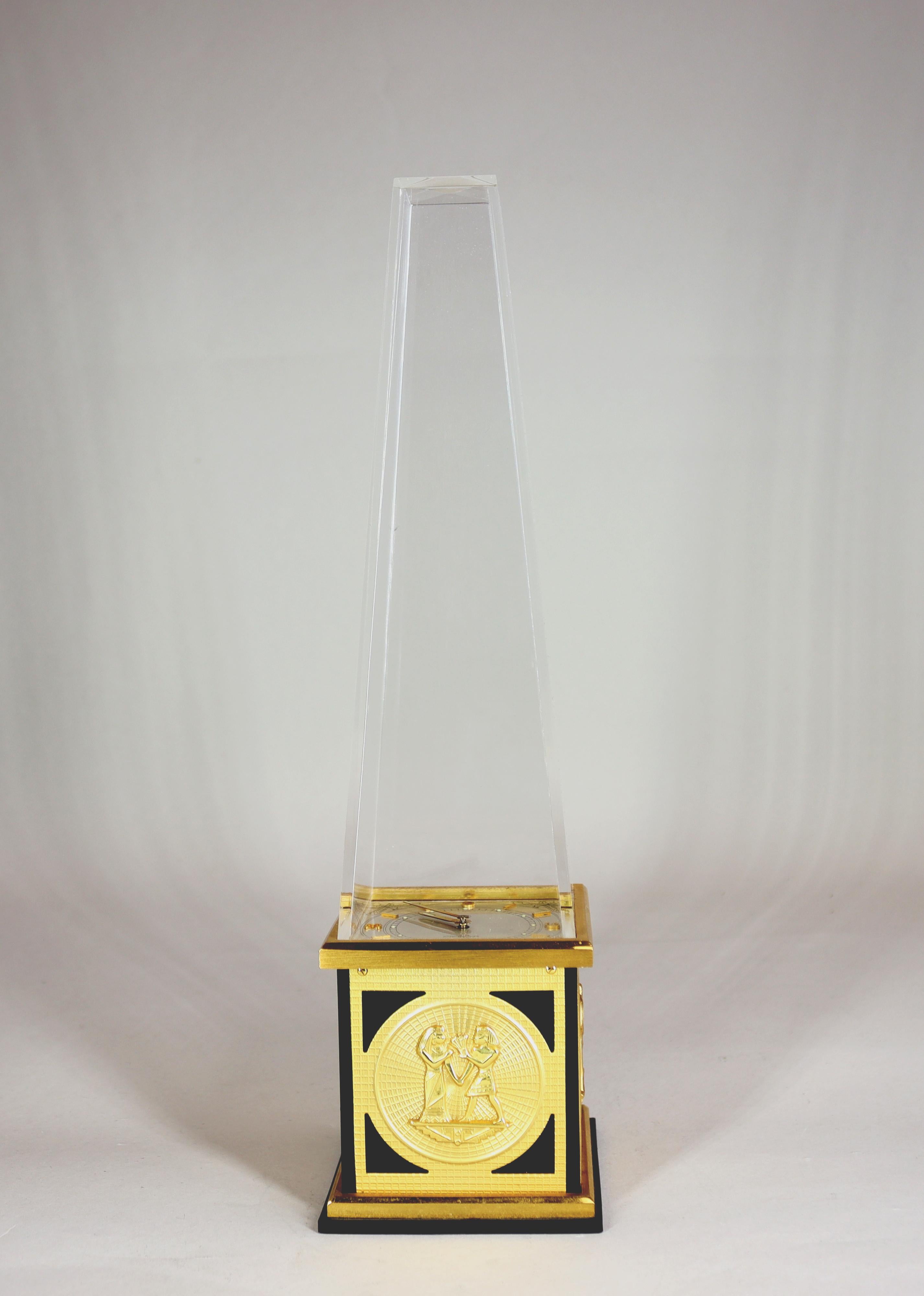 Pendule de bureau en forme d'obélisque égyptien fabriquée par LeCoultre avec un mouvement de 8 jours dans la base, un cadran argenté brillant, des chiffres et des bâtons dorés sous un obélisque en plexiglas. La base laquée noire est ornée de