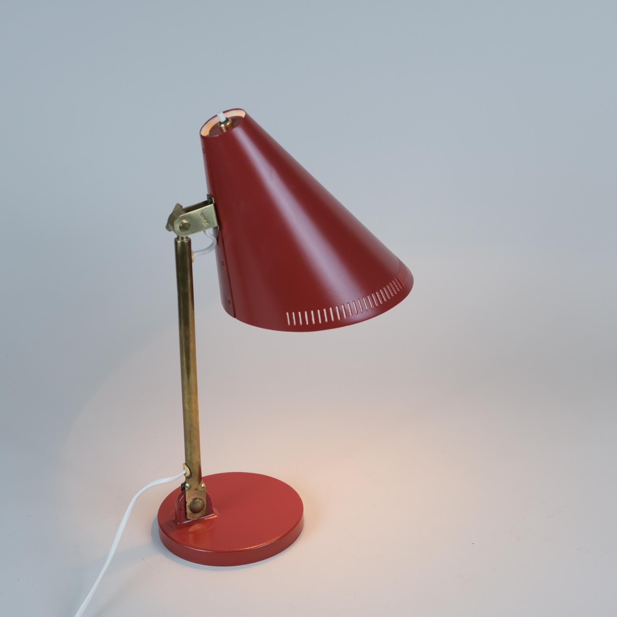 This table lamp model 9222 by Paavo Tynell is a time lasting and practical model feauturing a mixture of 3 different metal materials. In this model a firm brass stem supports an aluminum cone shade. The shade is in red and is adjustable for your