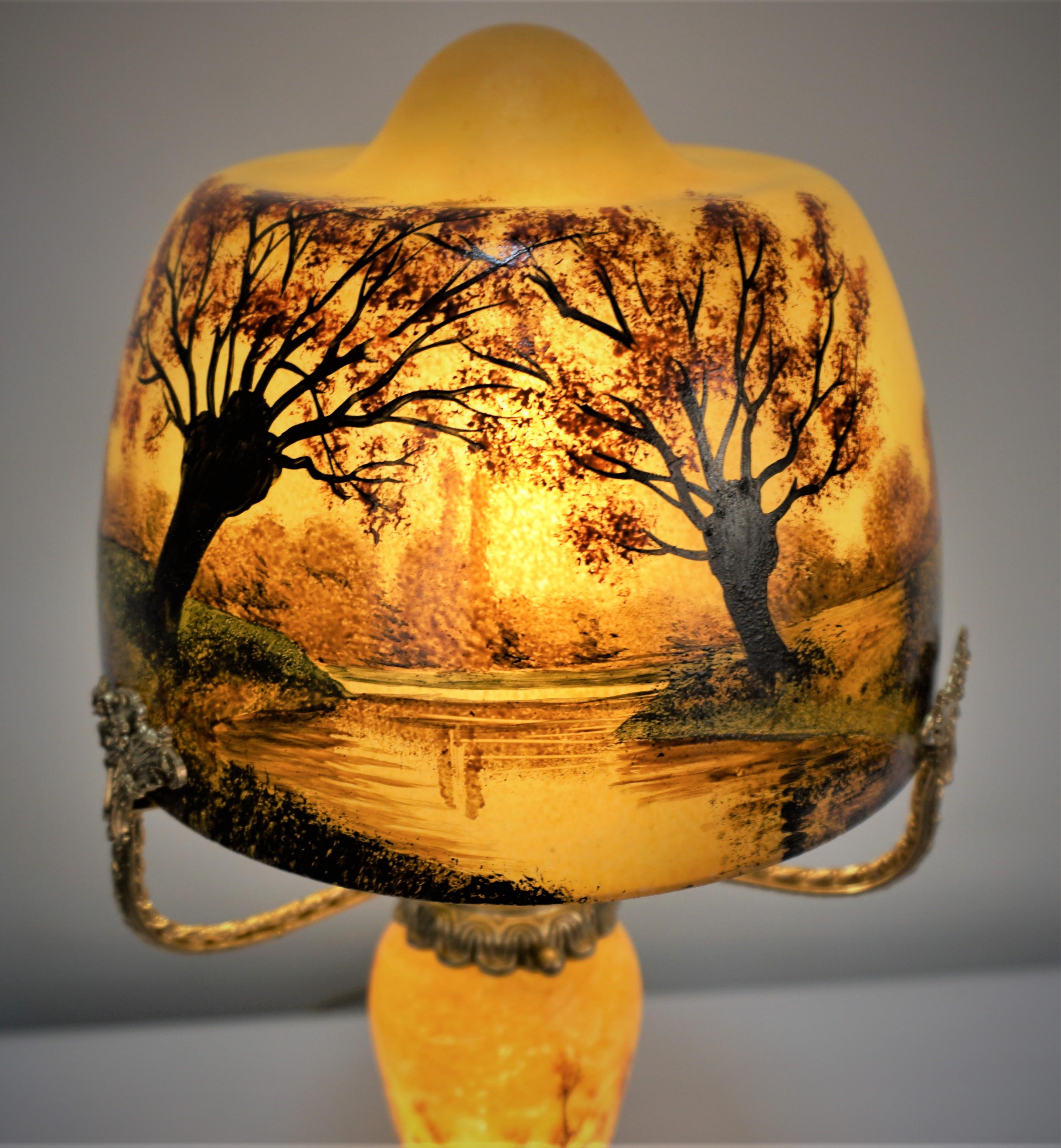 The clear glass body with yellow paint background with hand painted landscape on the shade as well as the base with metal arms and frame to support the shade signed Gauthier.
Two lights up and down.
   