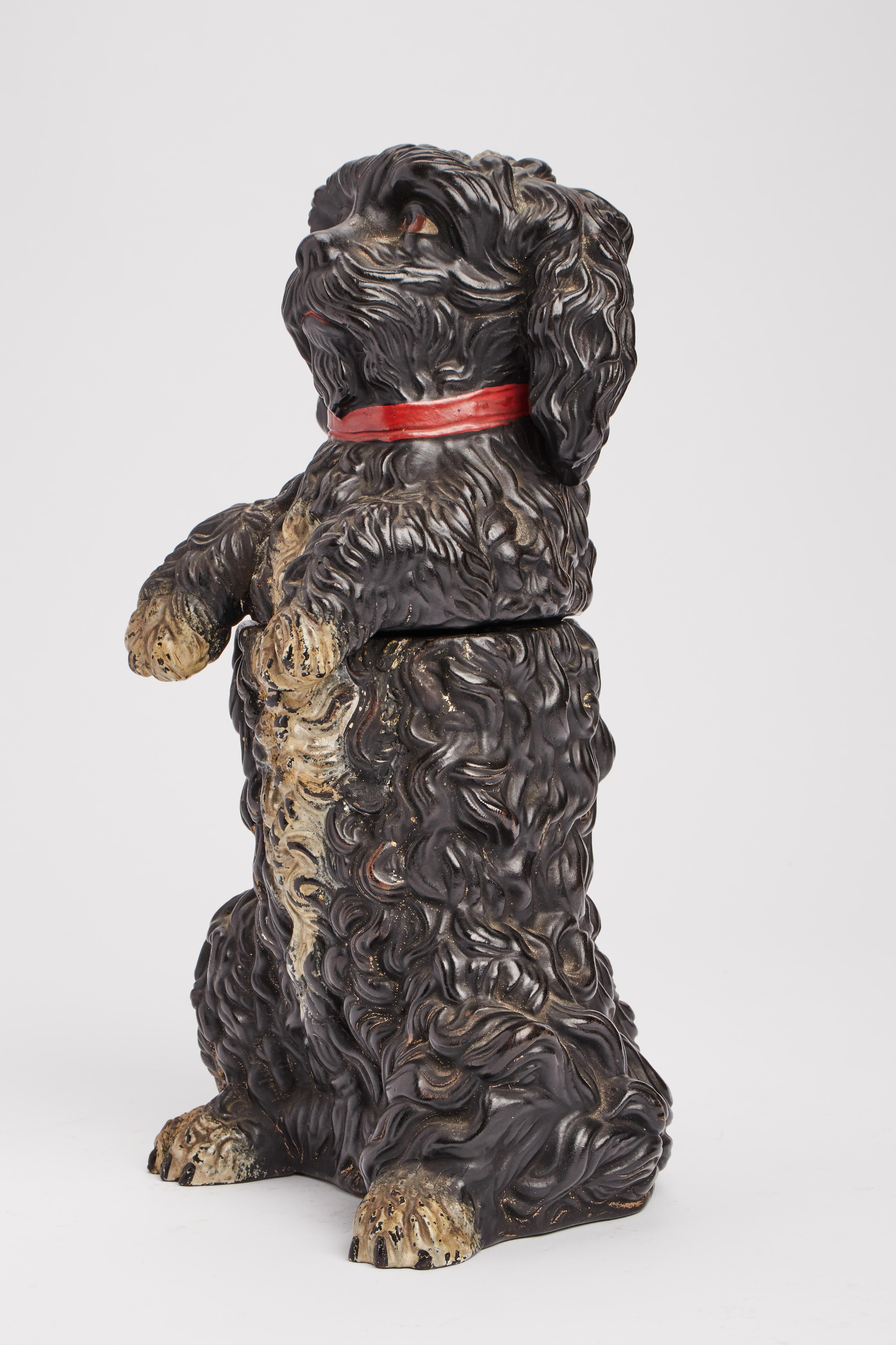Bemalte Terrakotta-Skulptur, die einen schwarzen Pudelhund mit rotem Halsband darstellt, der als Tabakhalter fungiert. Österreich um 1880.
