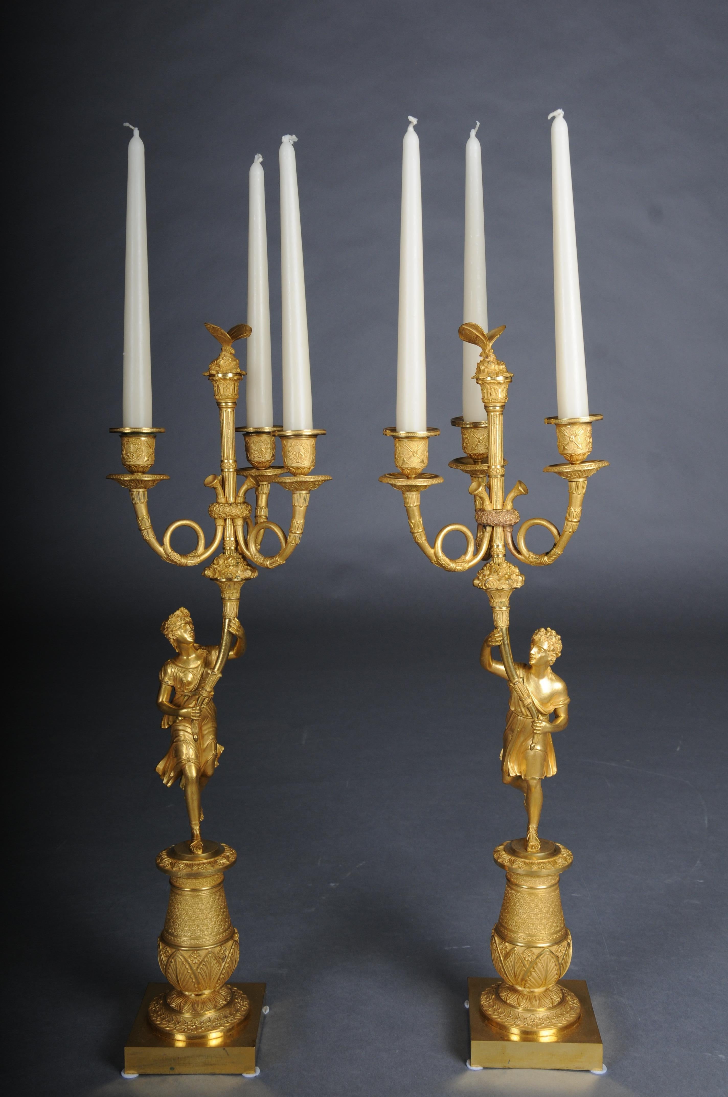 A pair (2) of figural Empire candelabra candles. Paris, 1815s

Gilt bronze. Recessed pedestal base with palmette and floral decoration on a square plinth. The pair, dressed in antique-style costumes, are depicted as candlestick bearers, each holding