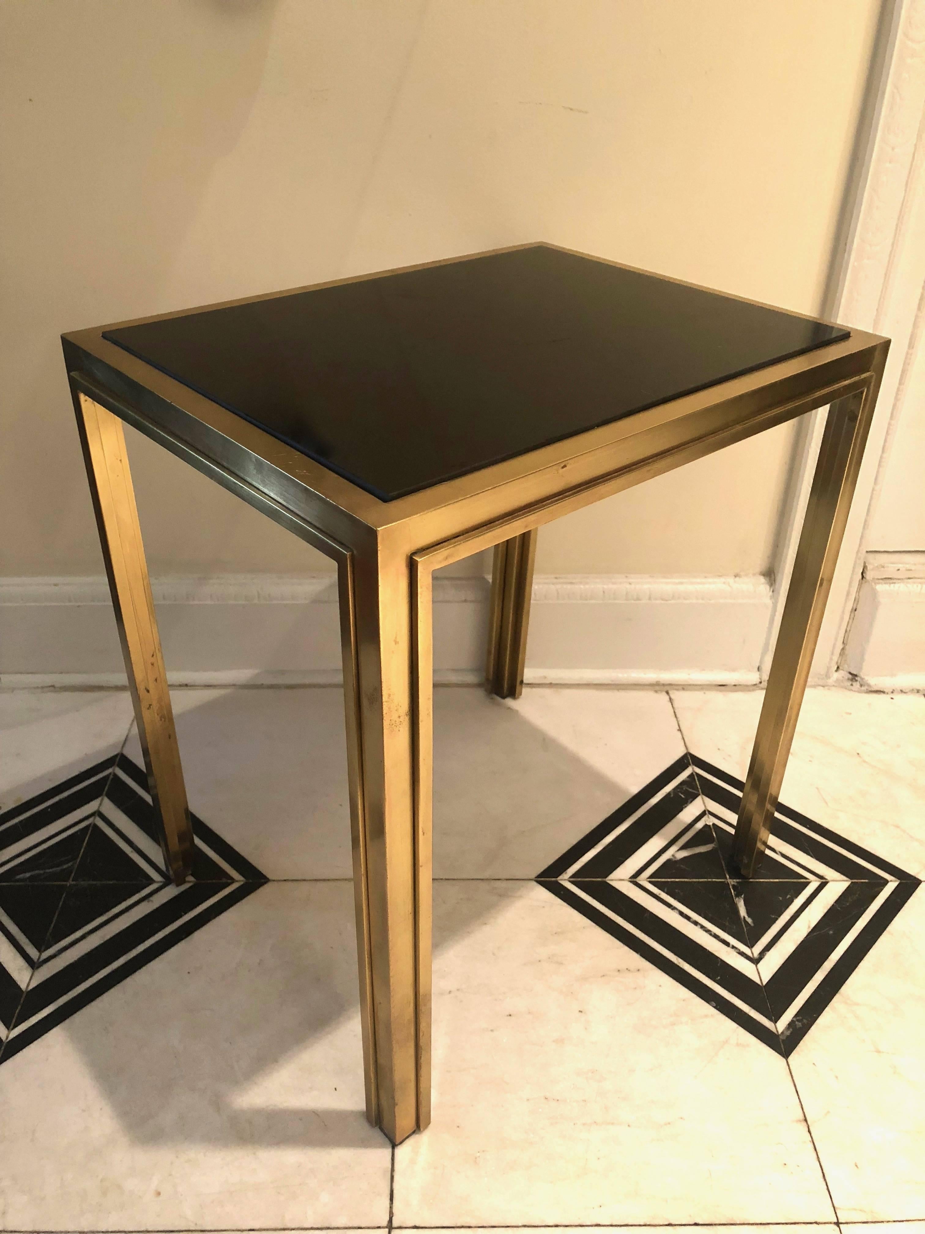 A pair of French deco side tables in original brass over bronze finish with a decorative trim along all of the inside edges. Each table has a black inset glass top. 
A total of Five tables available. 
 