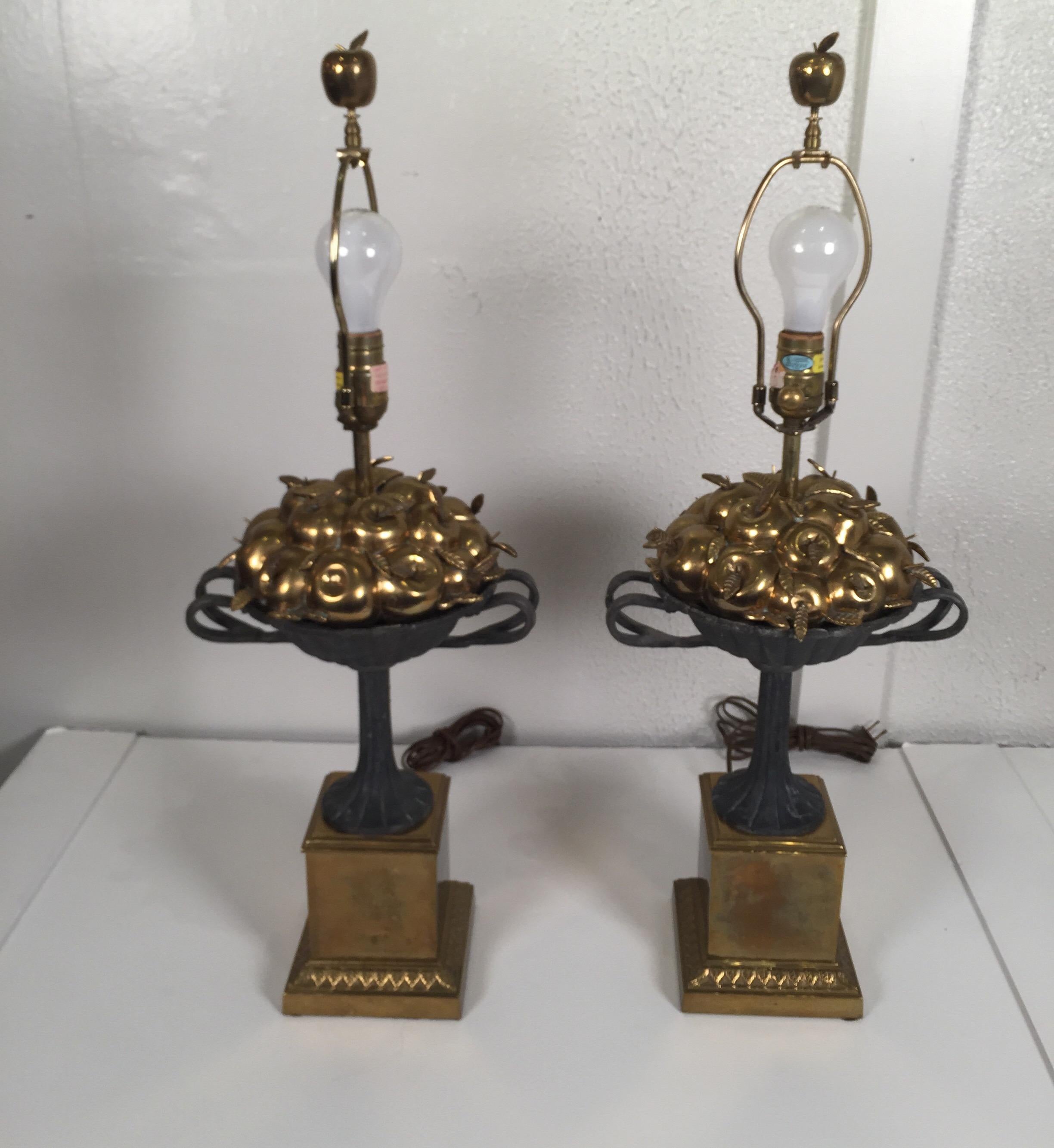 A whimsical pair of cast brass and iron lamps if the form of garden urns. The urns abundantly filled with apples in brass with iron urns with double handles. The finials on each are cast brass apples and original to the lamps. The simple drum shades