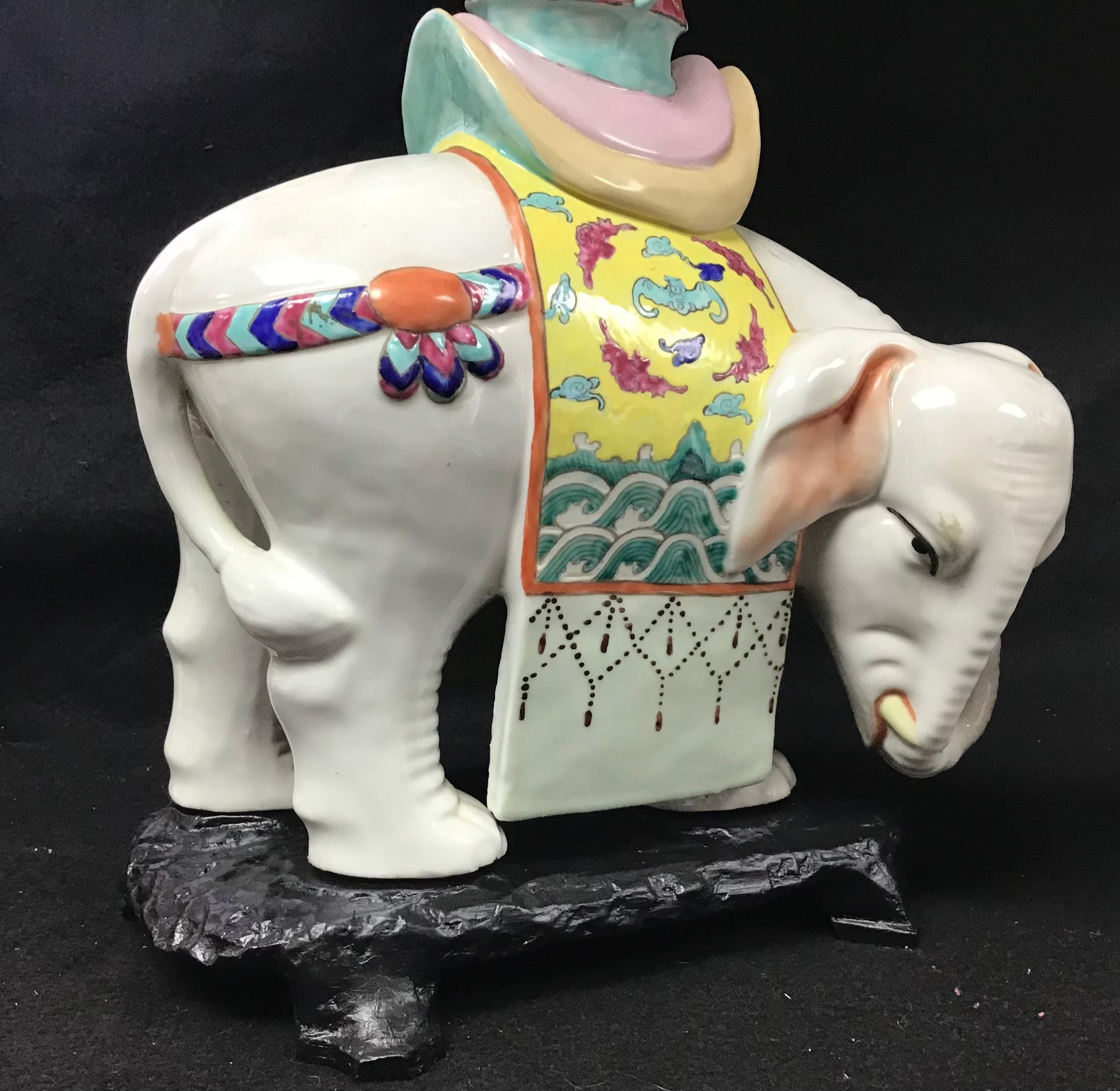 A large pair of Chinese export porcelain famille rose elephant candle holders. 20th century, white porcelain elephant wearing a riding blanket decorated with a Chinese universe pattern of mountain peaks, waves and clouds, and a saddle topped with a