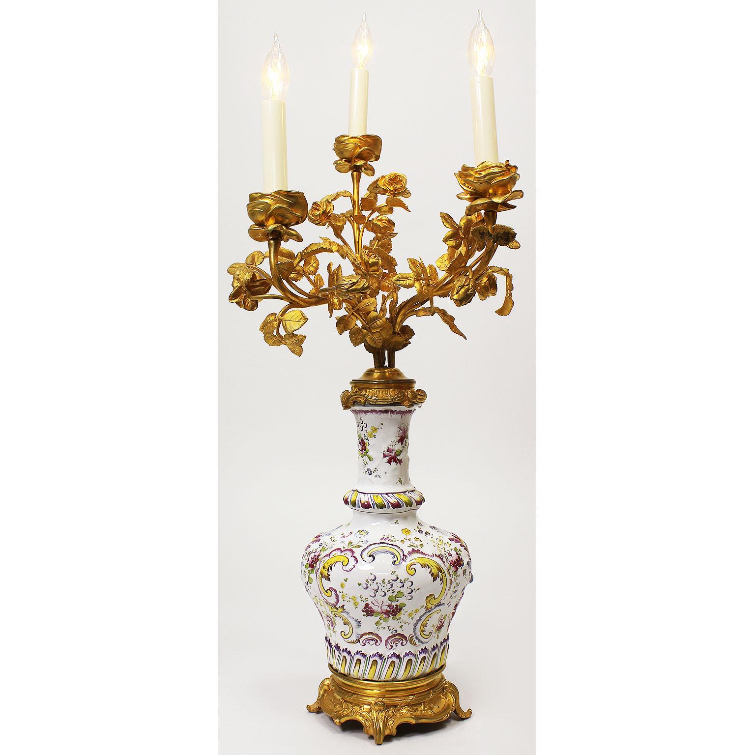 A fine pair of French 19th-20th century Louis XV style gilt bronze and Faience porcelain three-light candelabra table lamps. The ovoid porcelain urn hand decorated in floral burgundy, yellow and gold design, surmounted with an intricate three-light