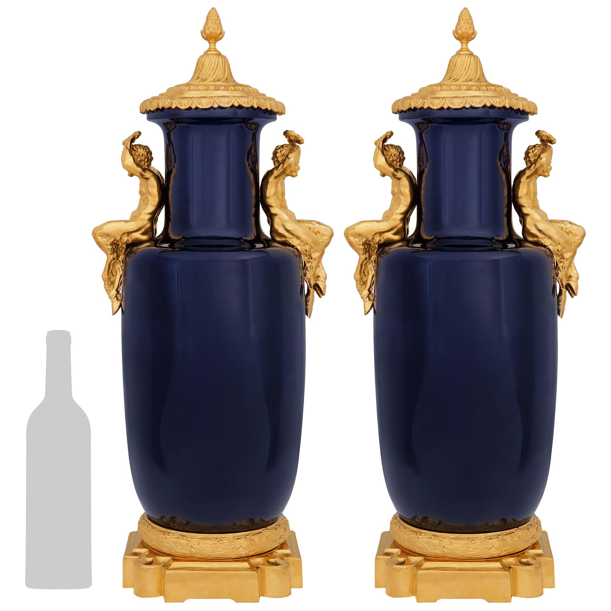 An impressive and large scale pair French 19th century Louis XVI st. Sévres Porcelain and Ormolu urns. Each stunning vase is raised on a handsome square Ormolu base with concave and rounded corners, and a top mottled edge. Atop of the base is a