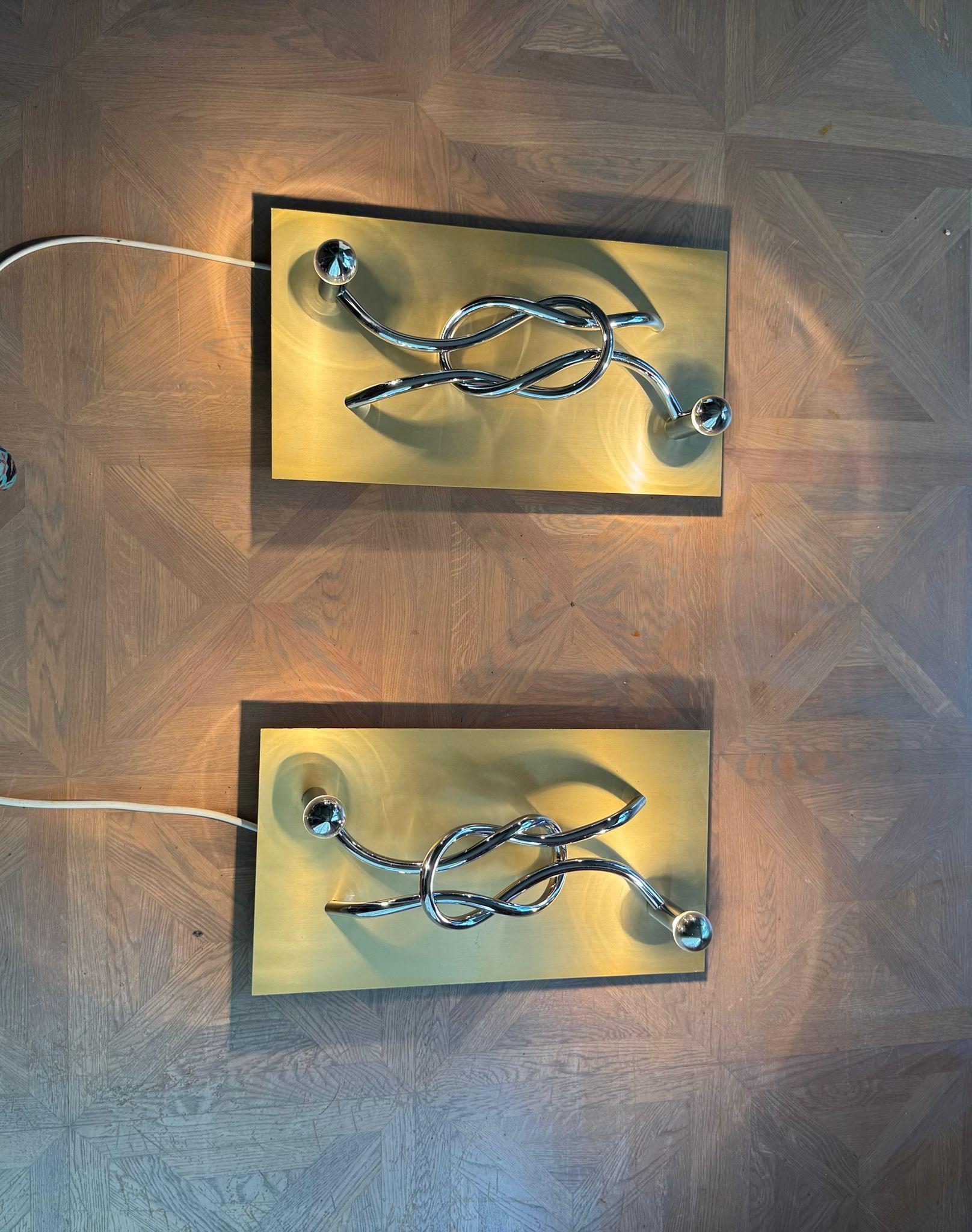A pair of Italian wall light panels, designed by Giacomo Benevelli in 1970, each with a silvered 'reef knot' design and two silvered bulbs, on gold finished panels. They have plugs to light them up which means that they can be placed anywhere in
