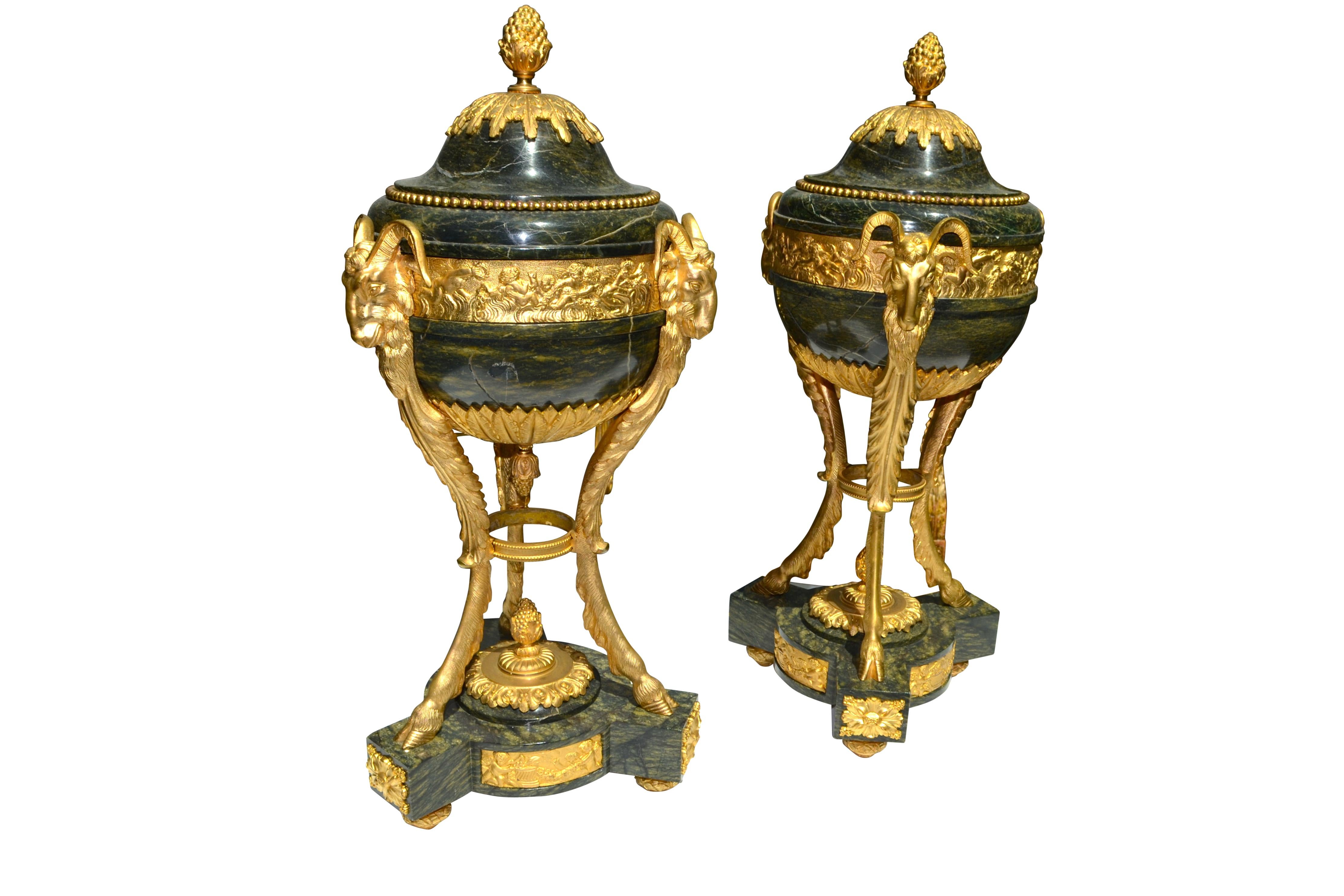 A pair of lidded urns in the Louis XVI style, the bronzes very much in the manner of the famous French sculptor Gouthiere. The tri-form base richly decorated with gilt bronze trim supports three 'legs' each terminating in a goat's head, which in