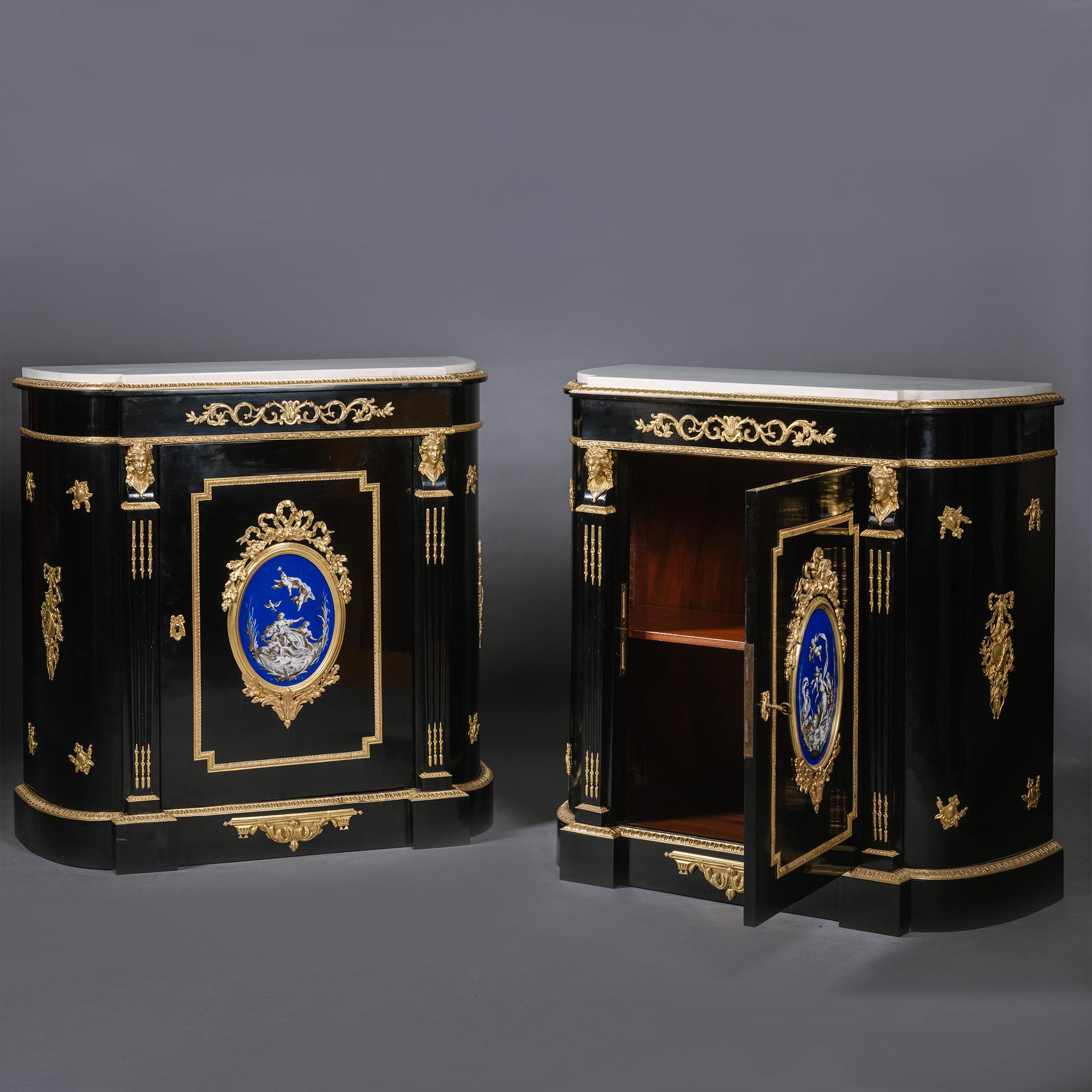A Pair Napoleon III Gilt-Bronze And Porcelain-Mounted Ebonised Cabinets, 'Meubles à hauteur d'appui'.

Each with 'D'-shaped inset white marble top above a frieze applied to the front with a scrolled gilt-bronze mount. The central doors with a