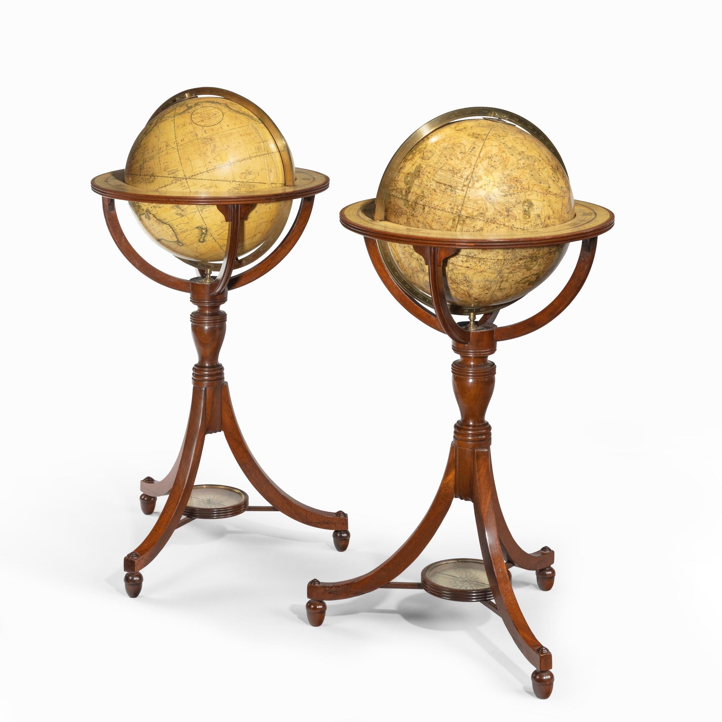 A pair of 12-inch floor globes by Cary, each set into a tripod walnut stand with a turned baluster support, outswept legs on acorn feet and stretchers centred on a replaced compass rose, the terrestrial globe stating ‘Cary’s New Terrestrial Globe