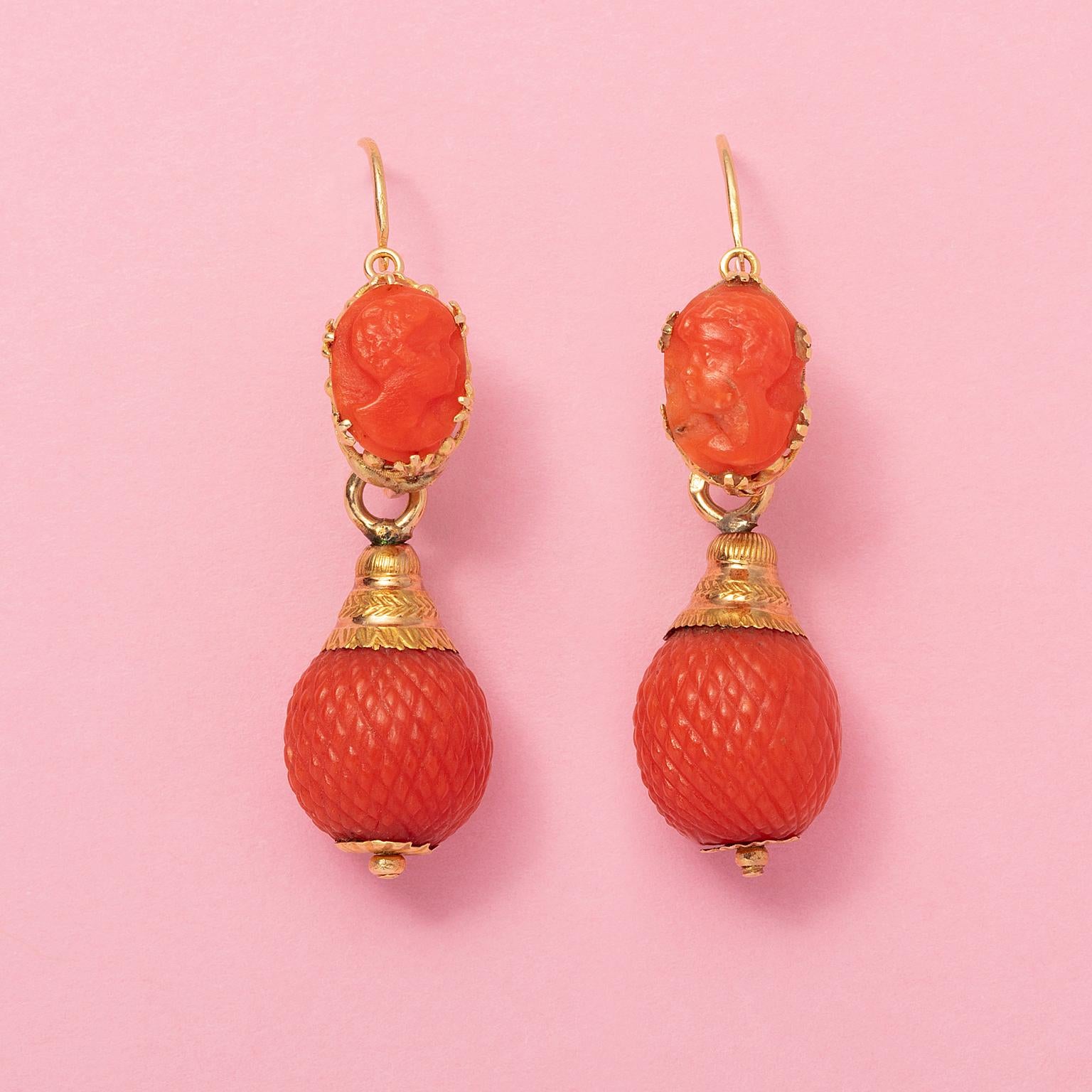 A pair of 18 carat yellow gold - day and night - earrings. A beautiful coral cameo of a lady set in a crown shaped chaton mounted on an elongated earring, underneath suspends a pineapple shaped coral bead, France, circa 1830, with a French