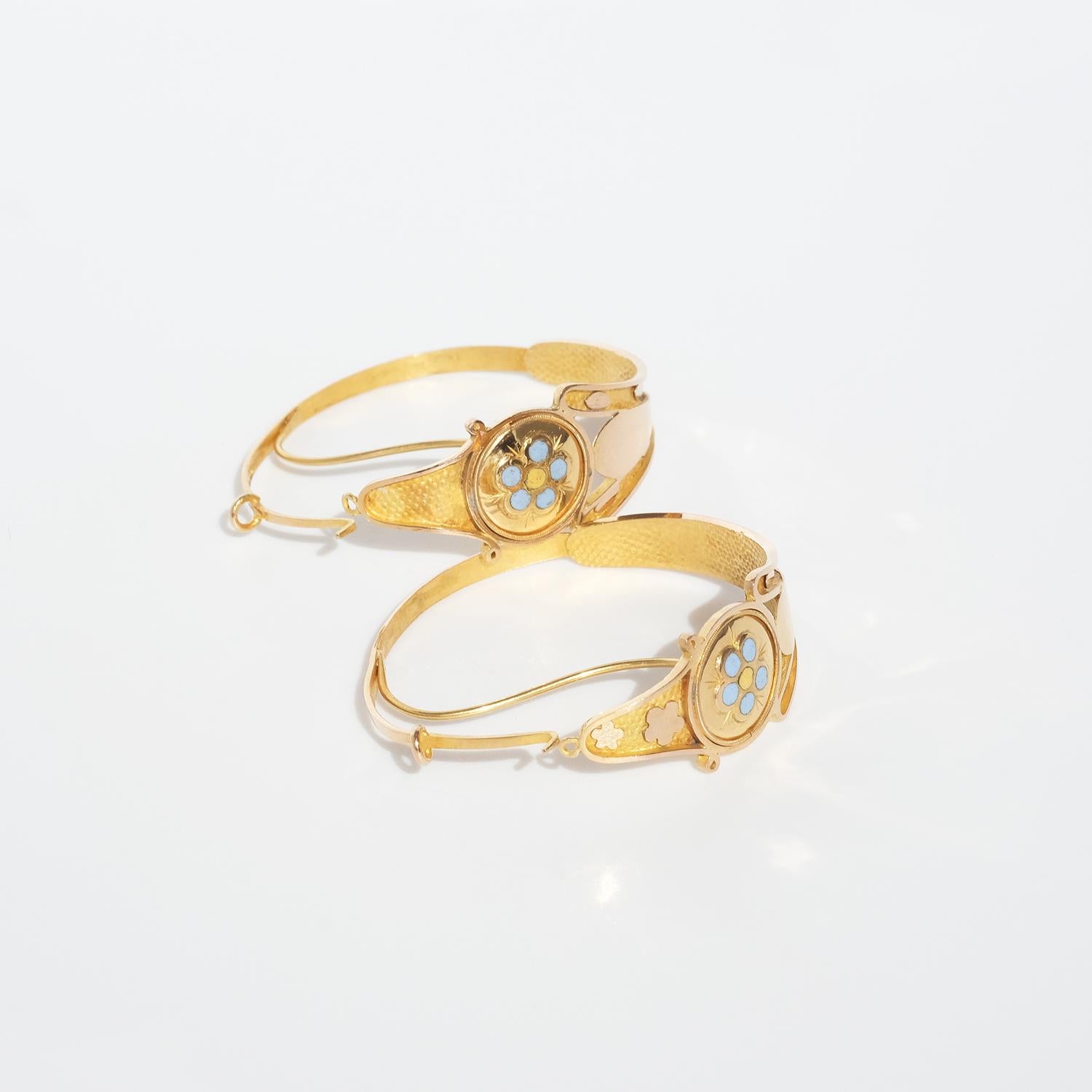 These 18 karat gold creole earrings are decorated with engravings, light blue and yellow enamel as well as with gold drops and small flowers. The earrings opens and closes with a hinged mechanism by a pin that shall be threaded through the ear and