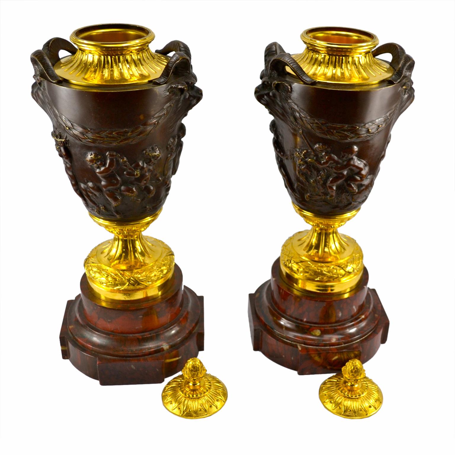 A pair of 19th century French lidded gilt bronze and patinated bronze urns after a popular model by the 18th century sculptor Clodion. The lids and circular urn bases are gilded and sit on a circular stepped griotte marble base. The patinated body