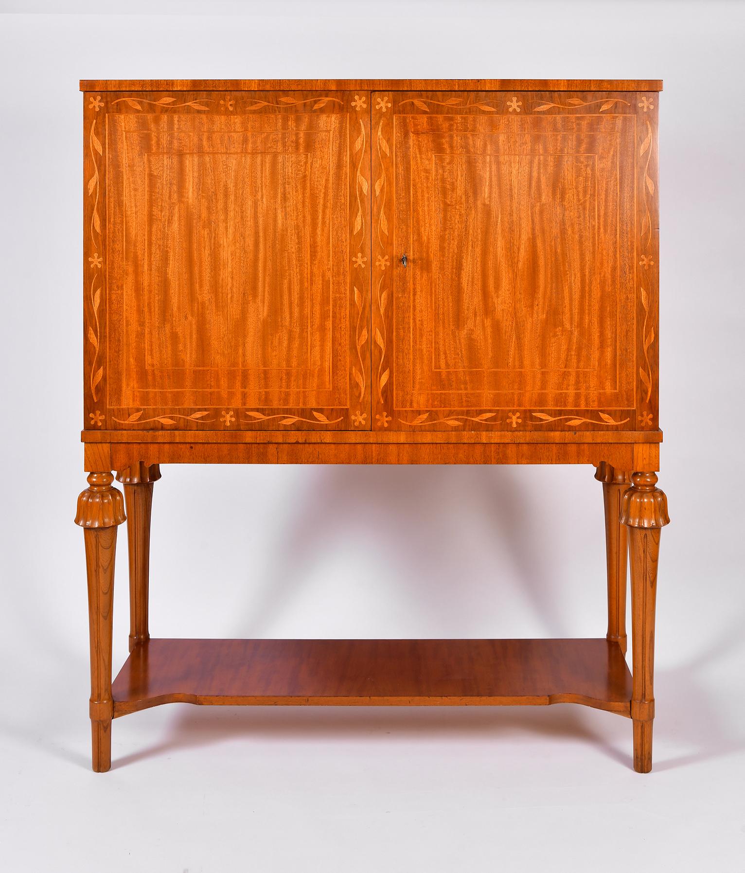 A pair of mahogany cabinets on stand, with floral marquetry, the cabinets with two doors revealing a fitted bookmatched ash veneer interior with drawers and shelves, resting on four carved legs, with shaped rails and lower shelf.
With its original