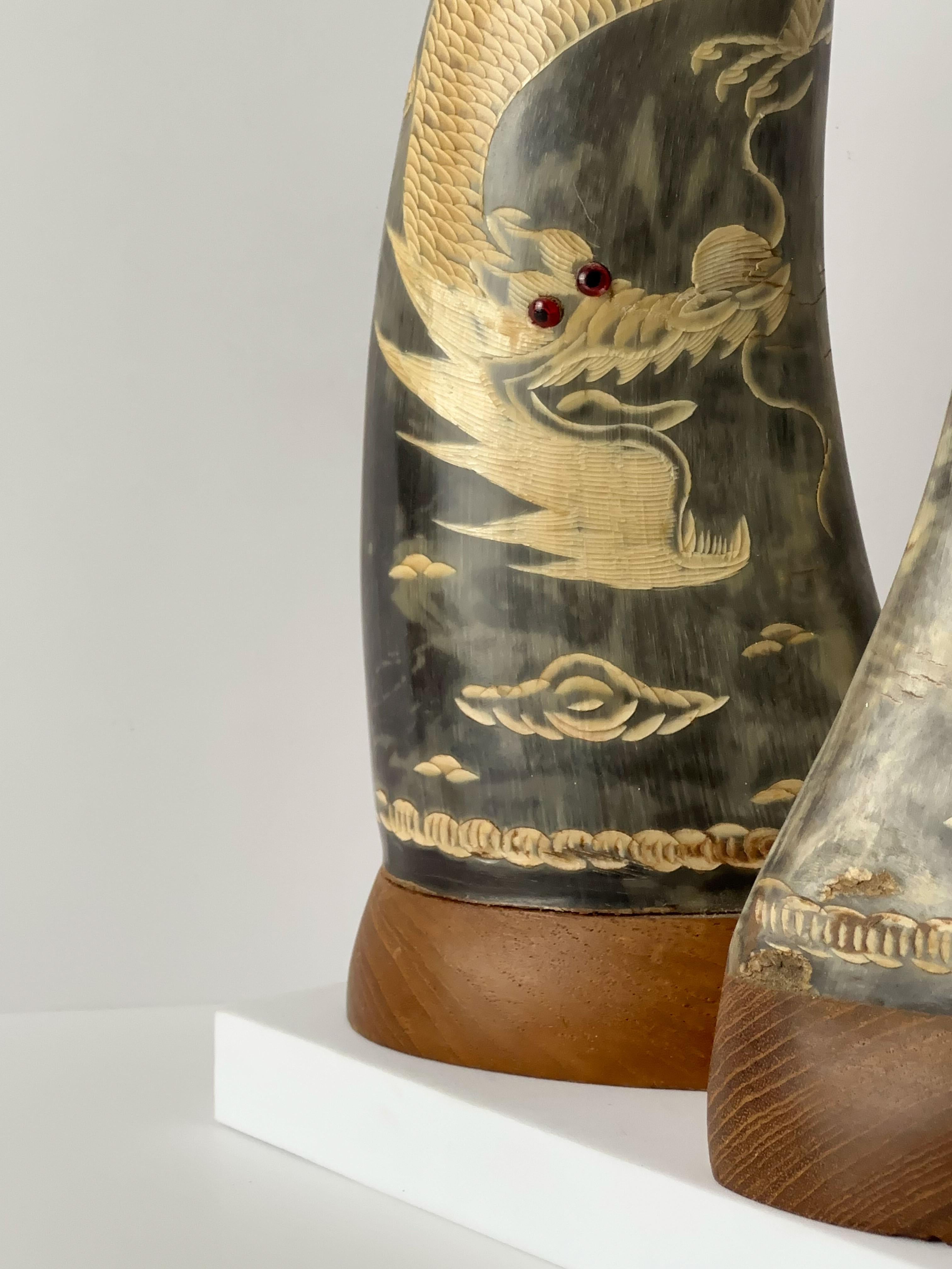 A pair of decorative Chinese water buffalo horns, hand-crafted in China around the 1950s. Each horn has been intricately hand-etched with a highly detailed dragon meandering across its surface. The etching reveals the lighter, bare tone beneath the