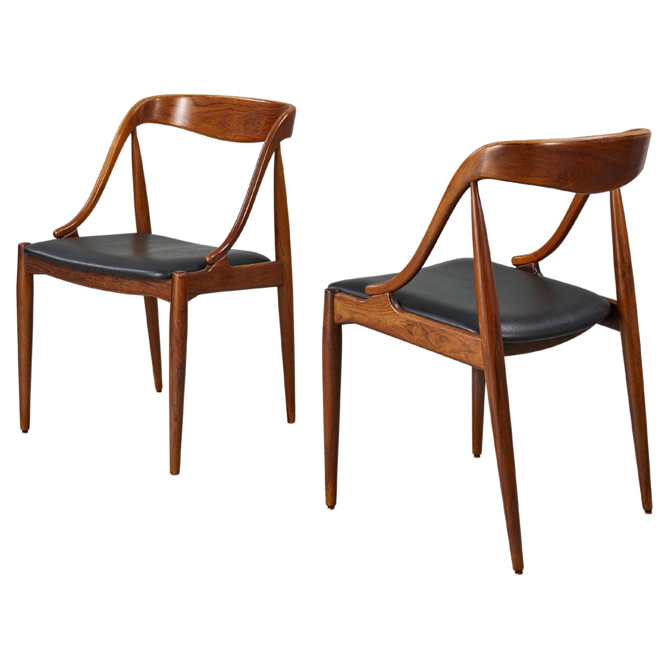 Offering a pair of Johannes Andersen-designed curved dining chairs for Uldum Møbelfabrik Denmark, these Scandinavian Modern classics are carved from solid teak wood. Symbolizing Danish Mid-Century Modern Design, they boast exquisite curves and
