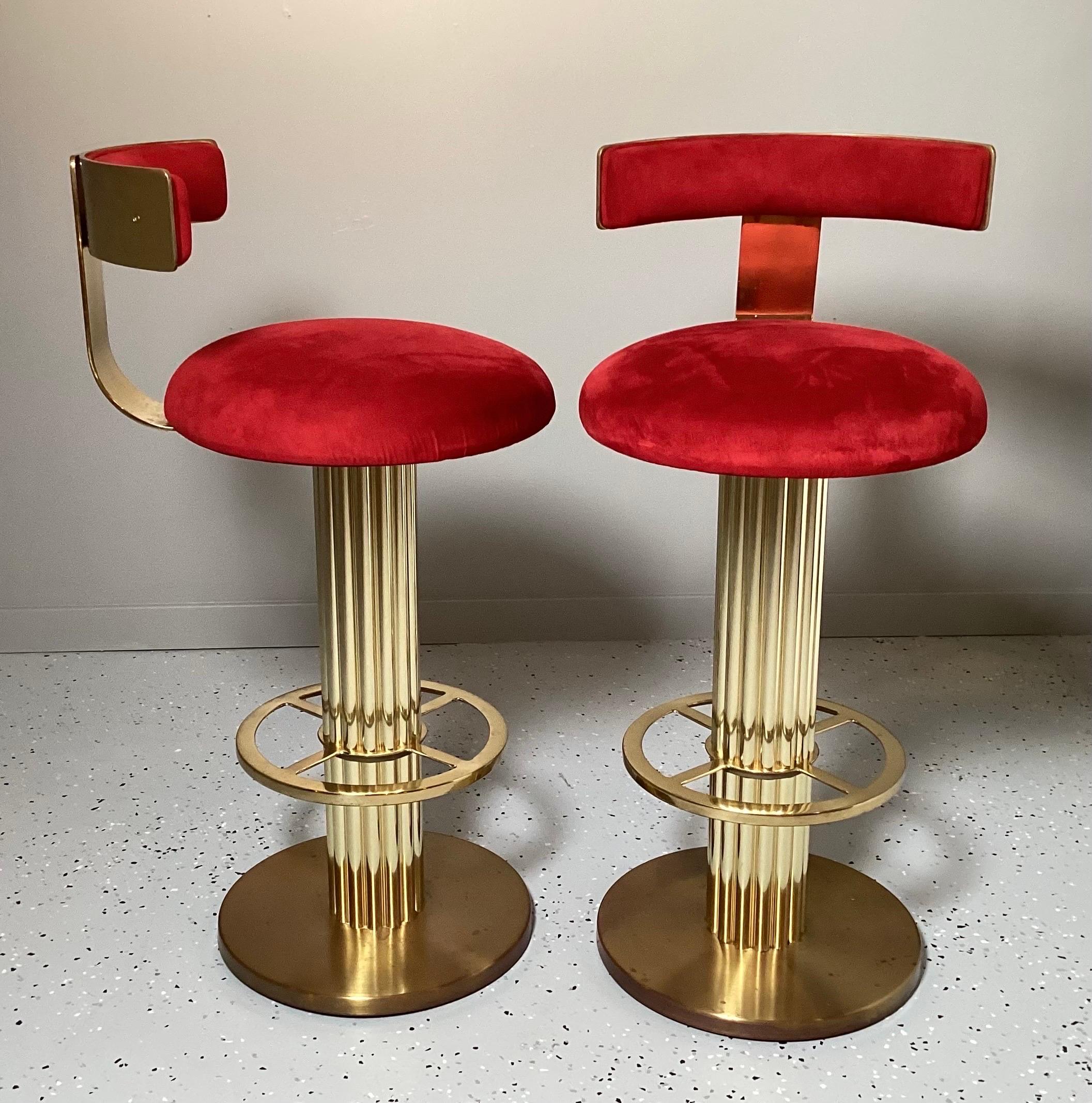 A pair of solid brass swivel bar stools. The very stylish stools made in the 1970's with an Art Deco inspired design. The original red velvet fabric is in good condition but can be easily changed to freshen these great bar stools