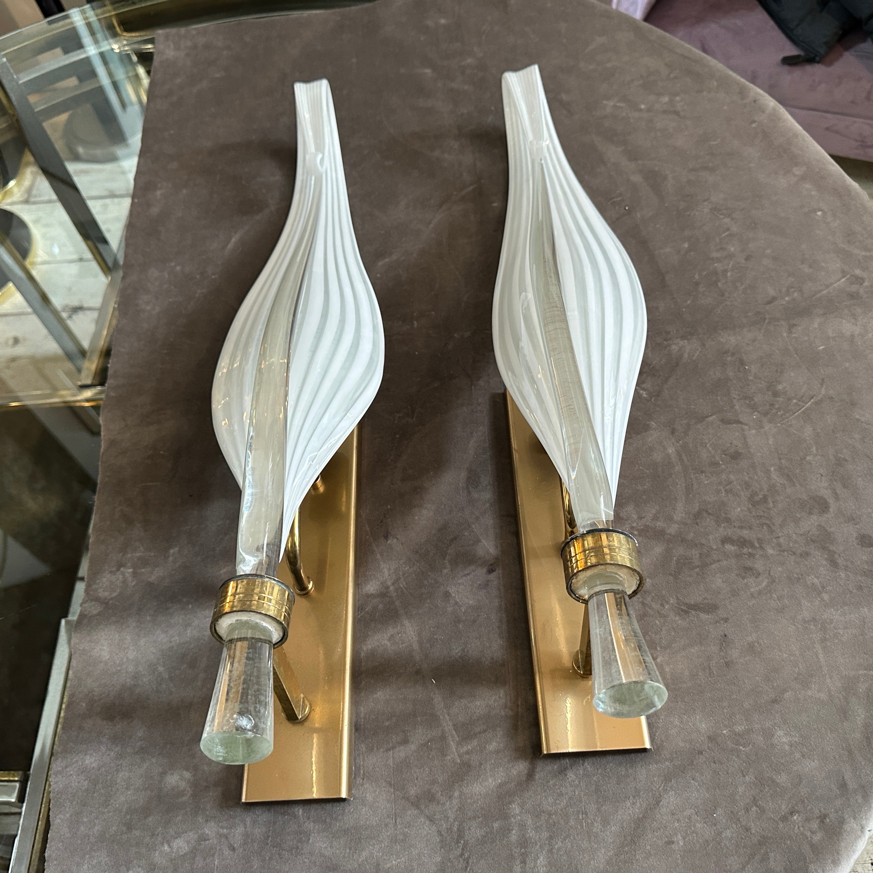 This pair of 1970s Mid-Century Modern Murano glass wall sconces by Franco Luce showcases the elegance and artistry of Italian glassmaking. Each sconce features an elongated, sculptural Murano glass shade with a gracefully tapered form, creating a