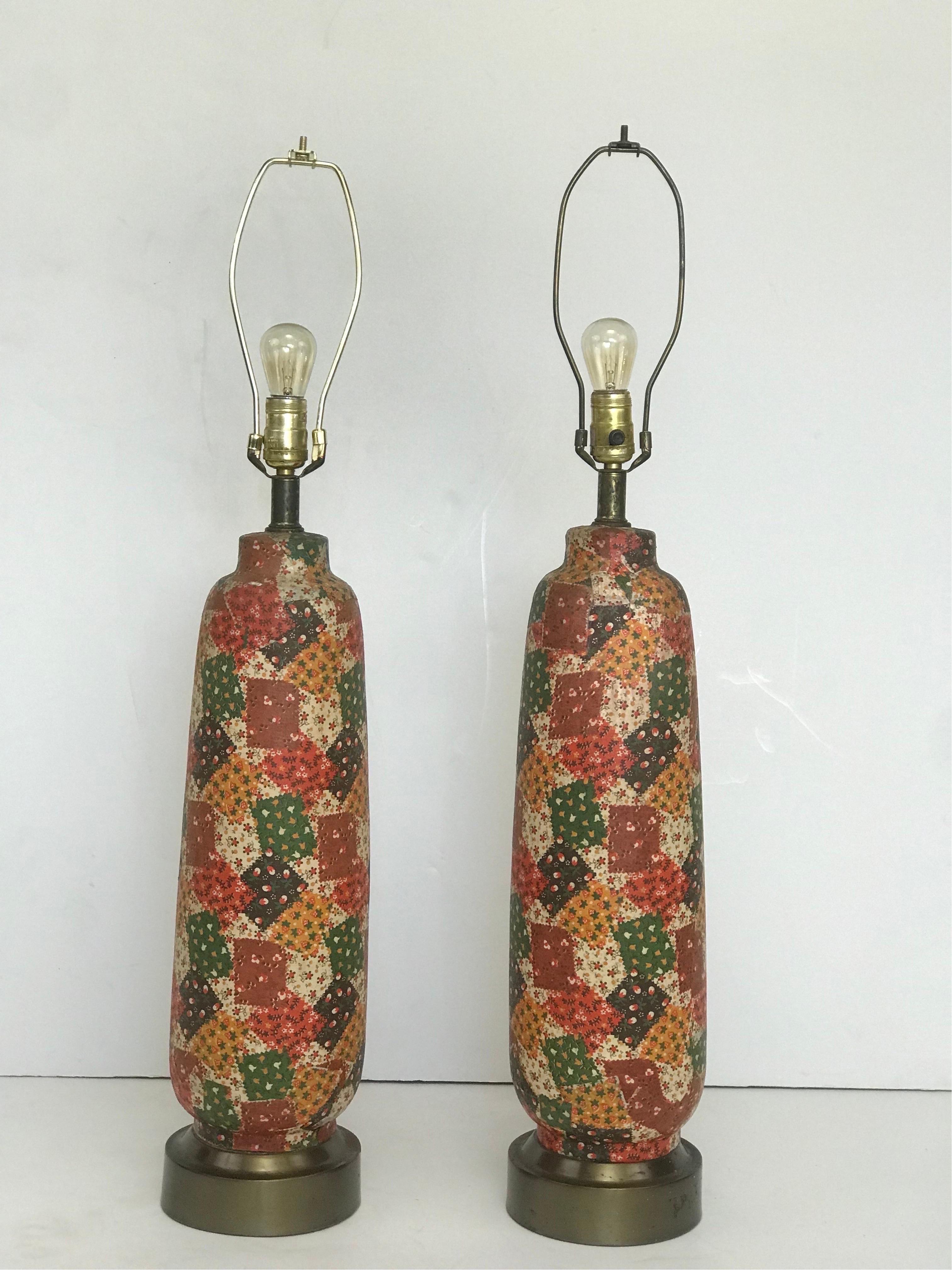 A unique pair of 1970’s spun metal table lamps with an applied papier-mâché style finish in a patchwork quilt theme printed natural material and set on a weighted metal base. 
Not wallpaper repurposed or a heat shrink, the material is natural in