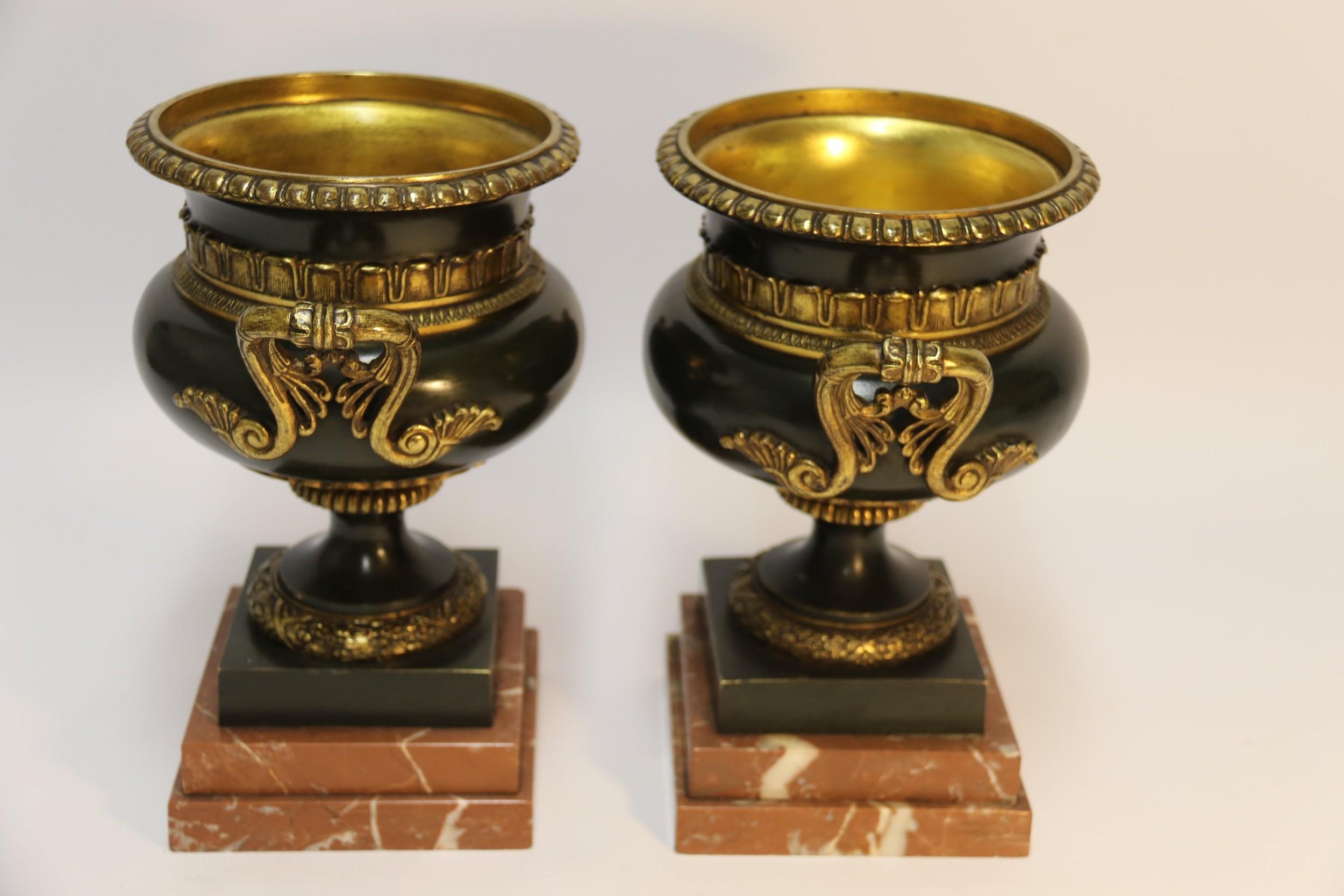 This stylish pair of decorative French 19th century bronze urns have a dark green patinated body with gilt bronze decorative collars and side handles which contrast and complement each other. They are mounted on double stepped rouge with white veins