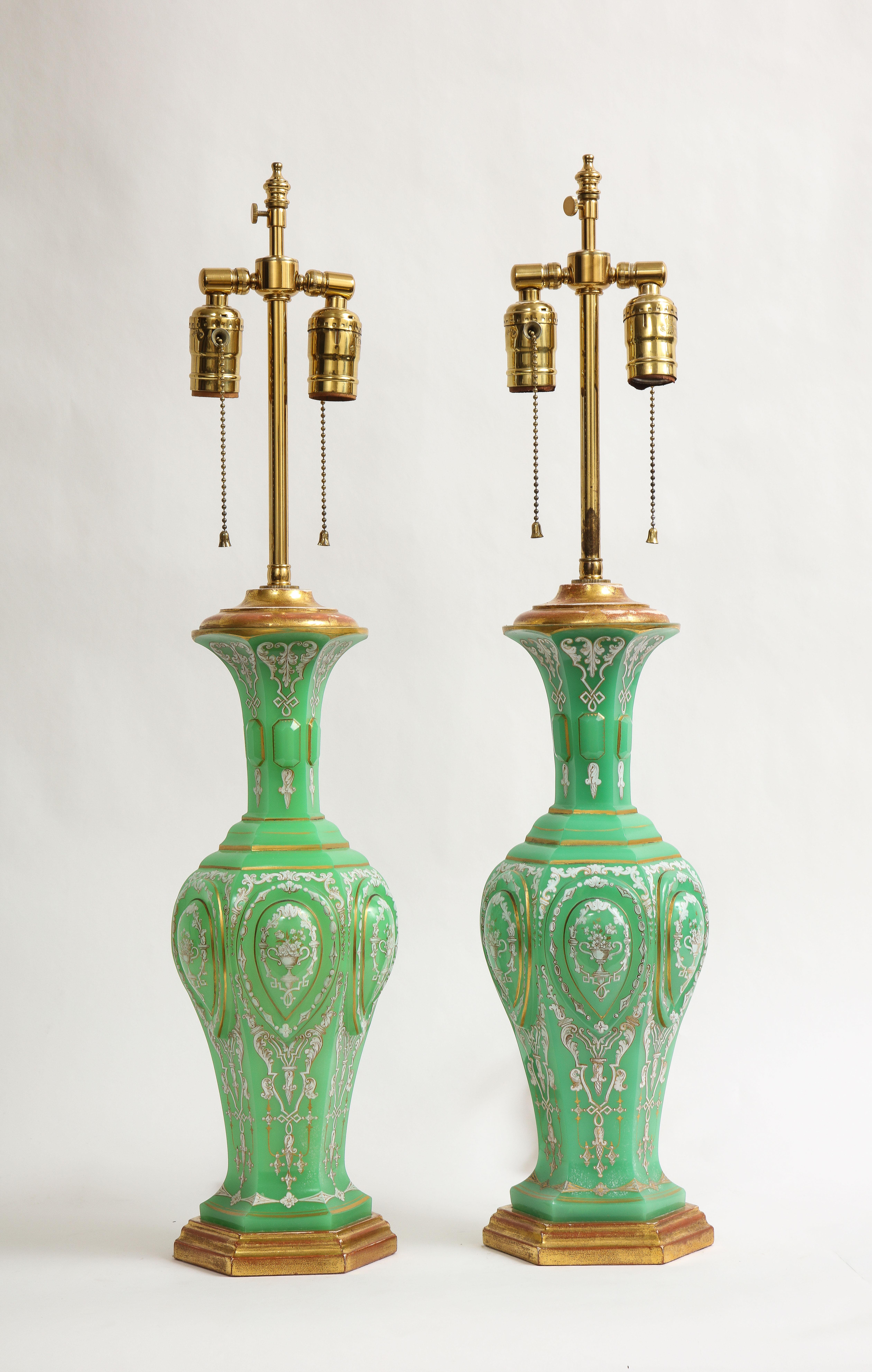 An incredible pair of 19th century French giltwood Emerald green opaline crystal and Enamel lamps, attributed to Baccarat. Each of these is made with the finest hand-cut French emerald green opaline crystal. The sides of each are beveled and have
