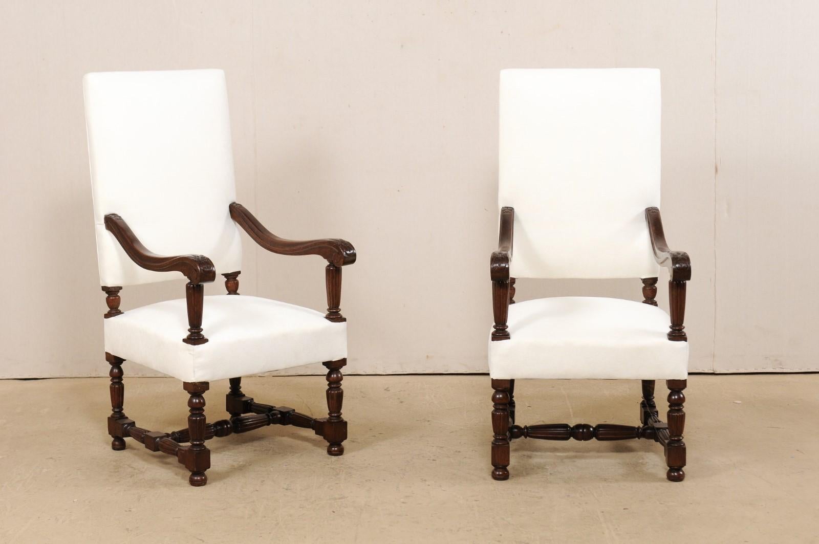 An Italian pair of carved-wood armchairs with newly upholstered fabric from the 19th century. These antique chairs from Italy each have a large rectangular-shaped back, with gracefully carved wooden arms that gently slope and terminate into scrolled