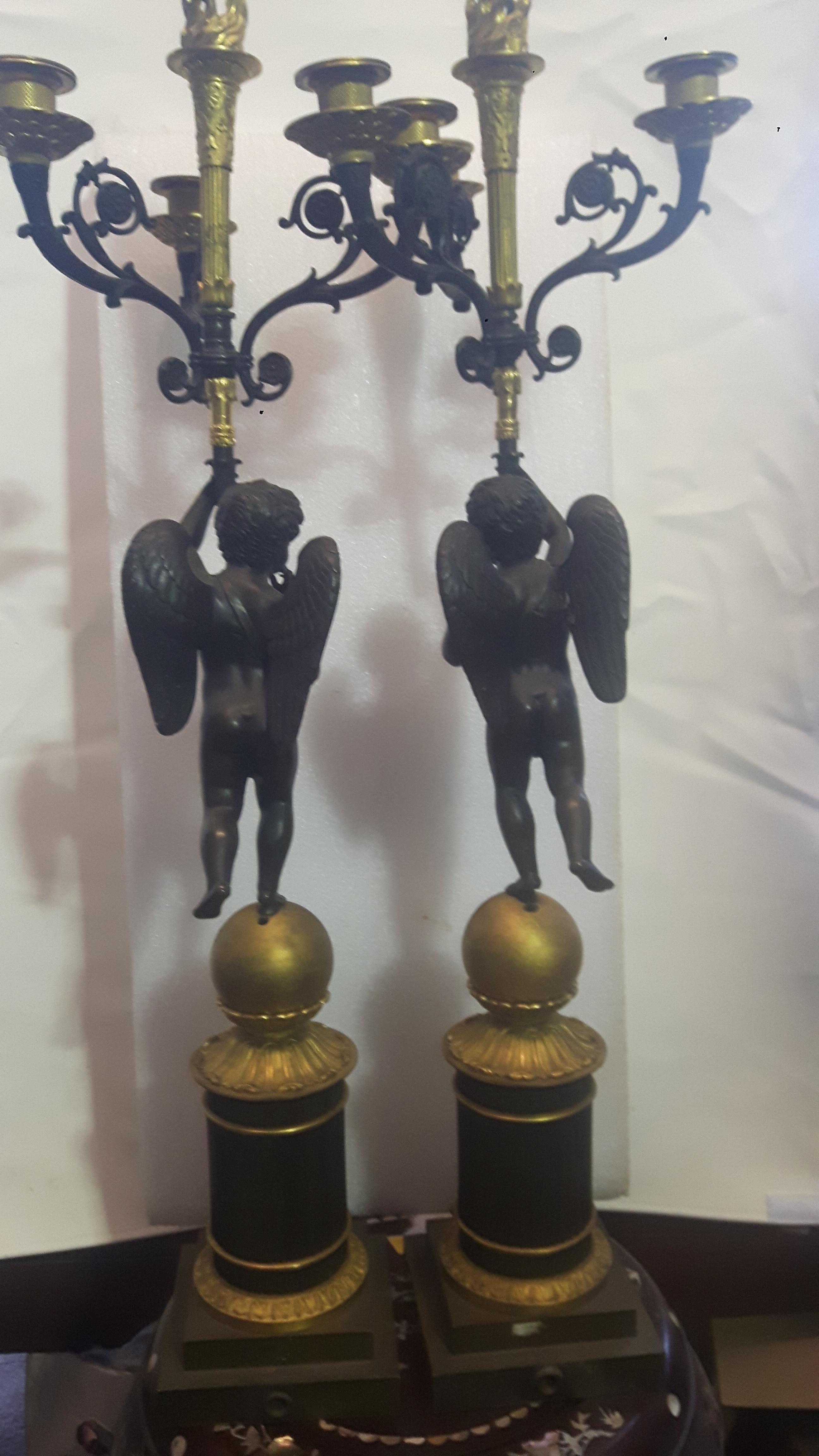 A pair of 19th century bronze and ormolu candelabra, with beaded nozzles held by well cast winged cherubs perched on spheres, ending on square plinth bases.