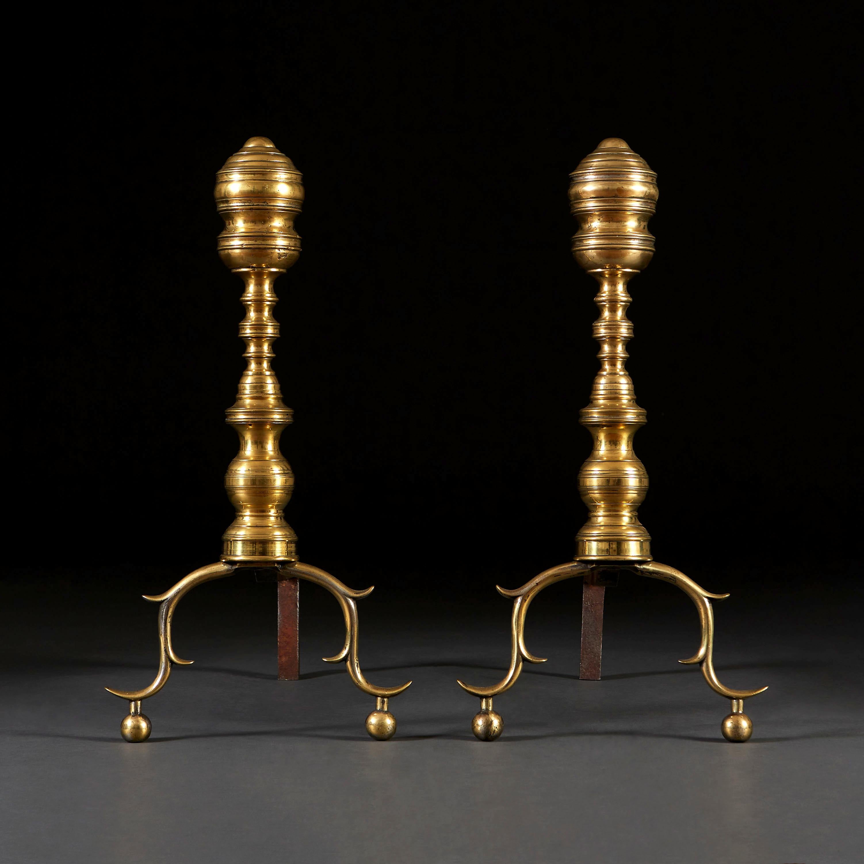 A pair of mid nineteenth century American brass and cast iron fire dogs, with turned uprights, and scrolled legs resting on ball feet.