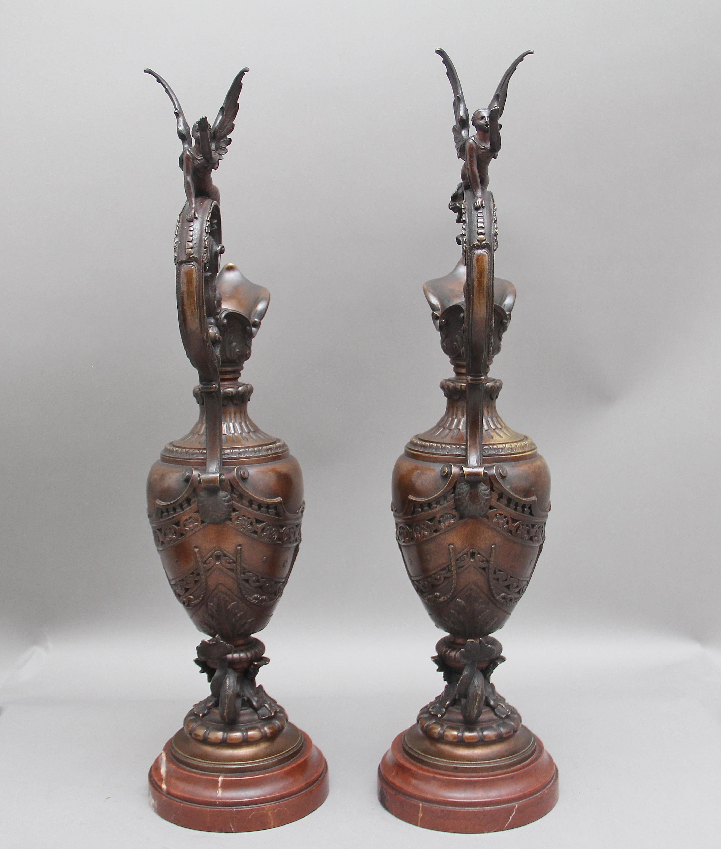 A decorative and rare pair of 19th century French bronze and marble ewers, having angels on top of the elegantly shaped handles, very fine detail throughout the ewers including lion masks and serpents, supported on rouge marble bases. Lovely patina