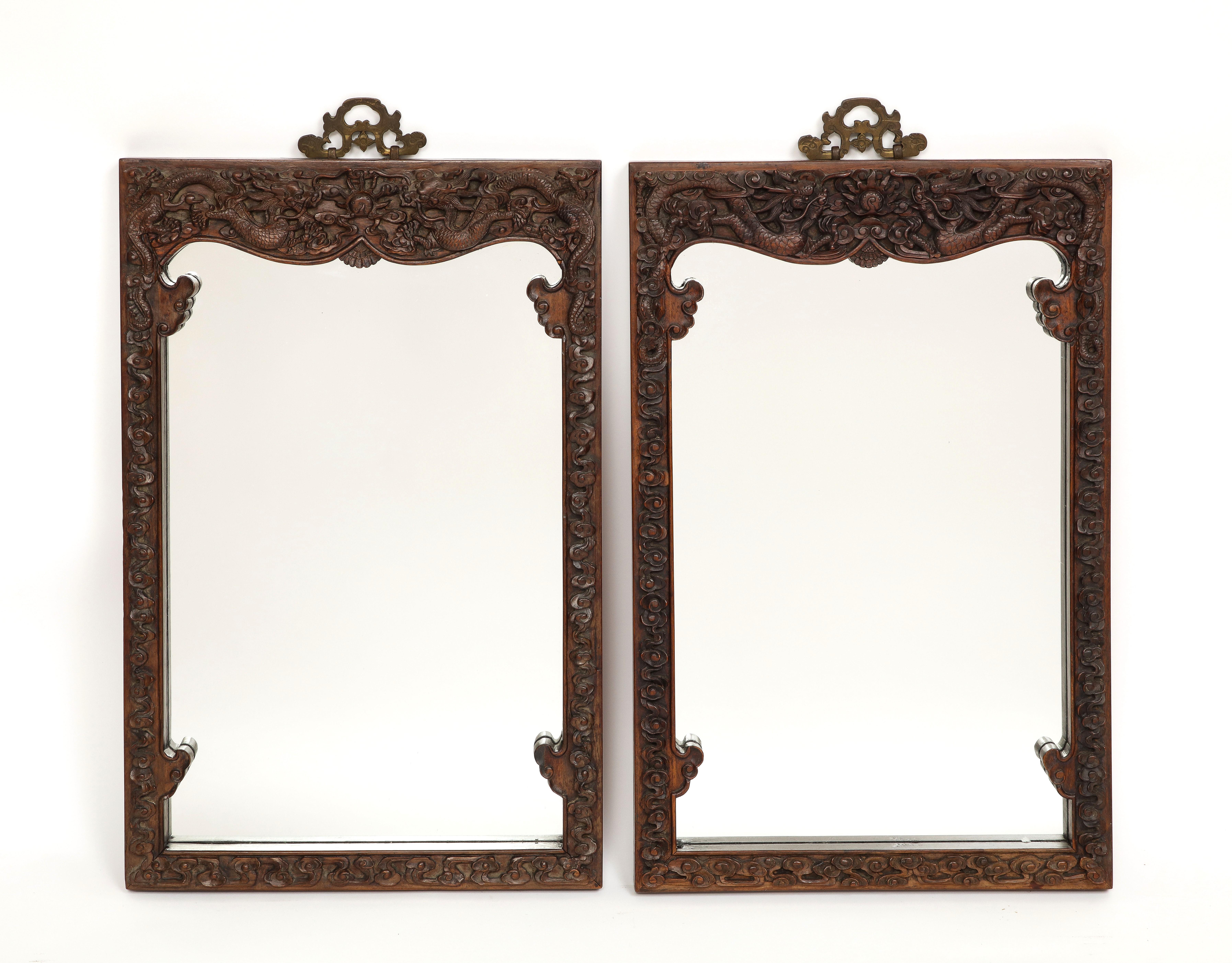 A pair of 20th century or earlier Chinese hardwood hand carved five-claw dragon mirrors. Each is hand carved with high relief Imperial five-claw dragons flying in the air. They also include hand carved elements of the sun, clouds, and flowers. Each