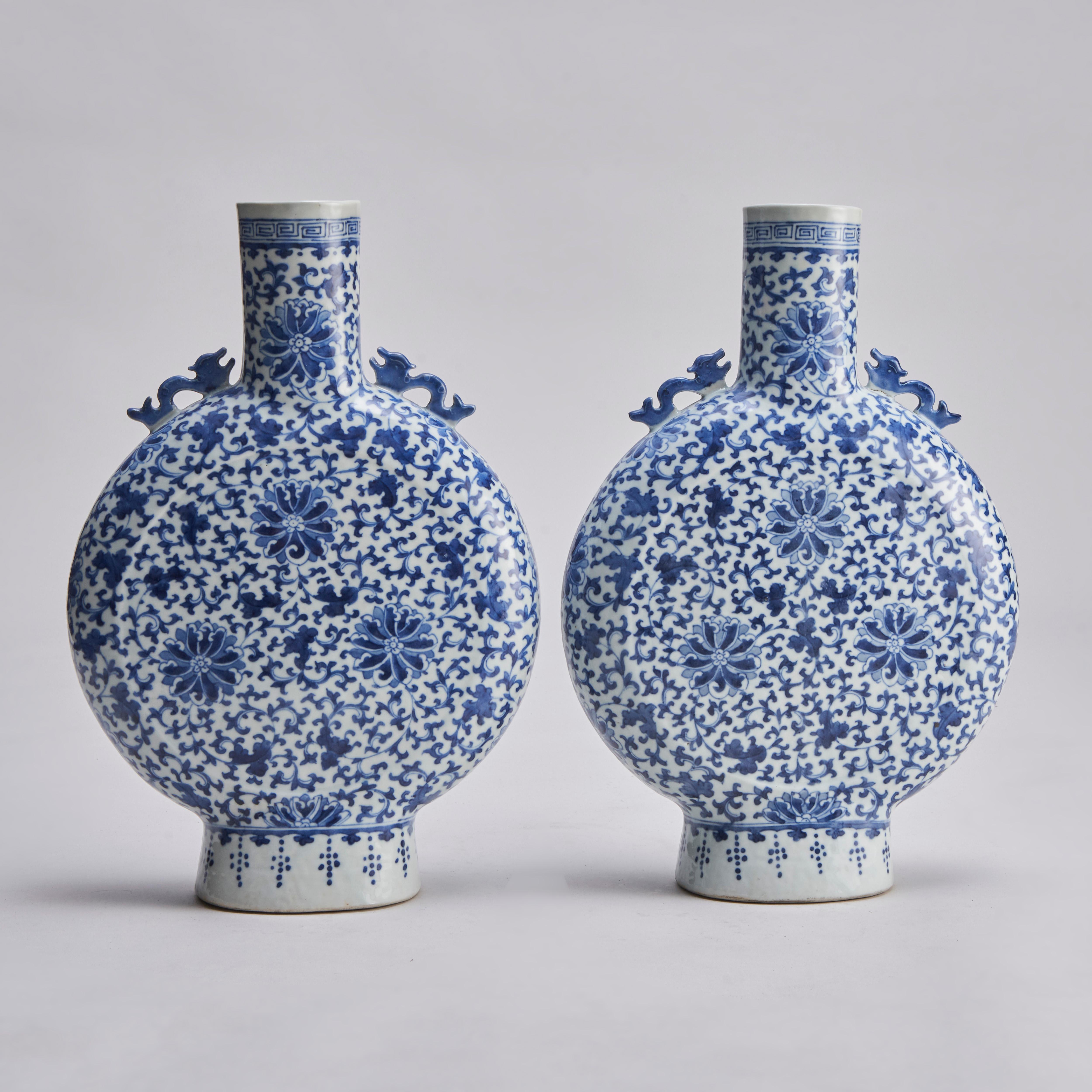 Paire de vases de lune/pèlerins chinois du XIXe siècle, de couleur bleu et blanc, avec un décor d'épaule de dragon moulé et un motif allover de fleurs de type clématite sur un fond feuillu.

Le col est orné d'une bordure en méandres Xiangyun et