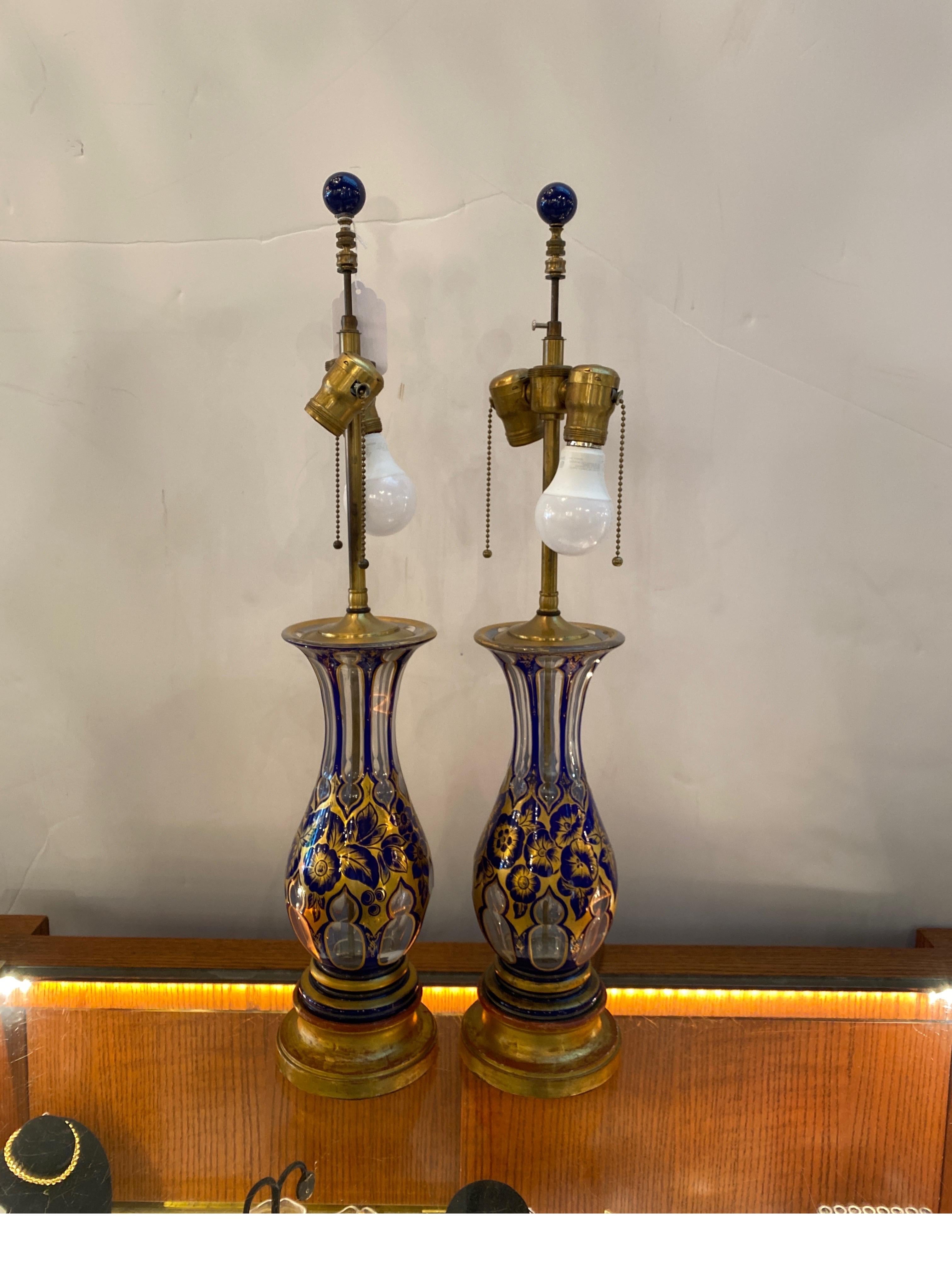 A pair or antique 19th Century cut glass vases as lamps.  The cobalt and gold top layer cut to a clear base.  The vases with early 20th Century gilt wood bases.  The center lamp rod with 2 working light sockets on pull chains.  The shades are for