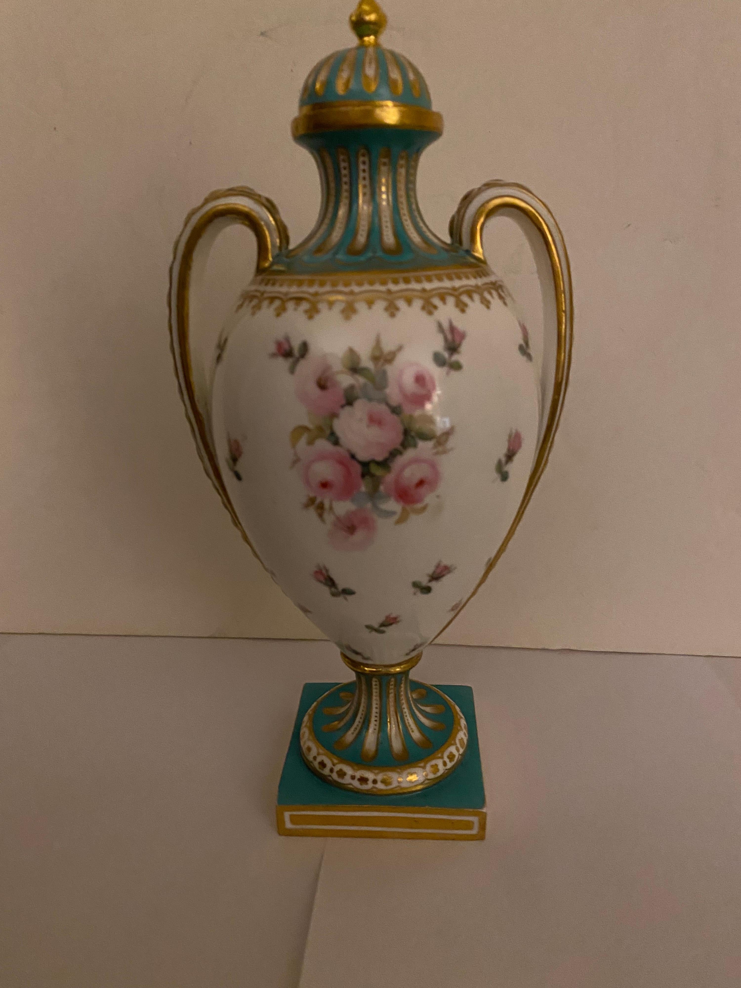 An elegant pair of 1860's hand painted English porcelain urns with lids, the diminutive urns with gilt decoration, are 8.5 inches tall to the tip of the finial on the urn. The domed lid resting on the floral bulbous body with pink rose cartouches on
