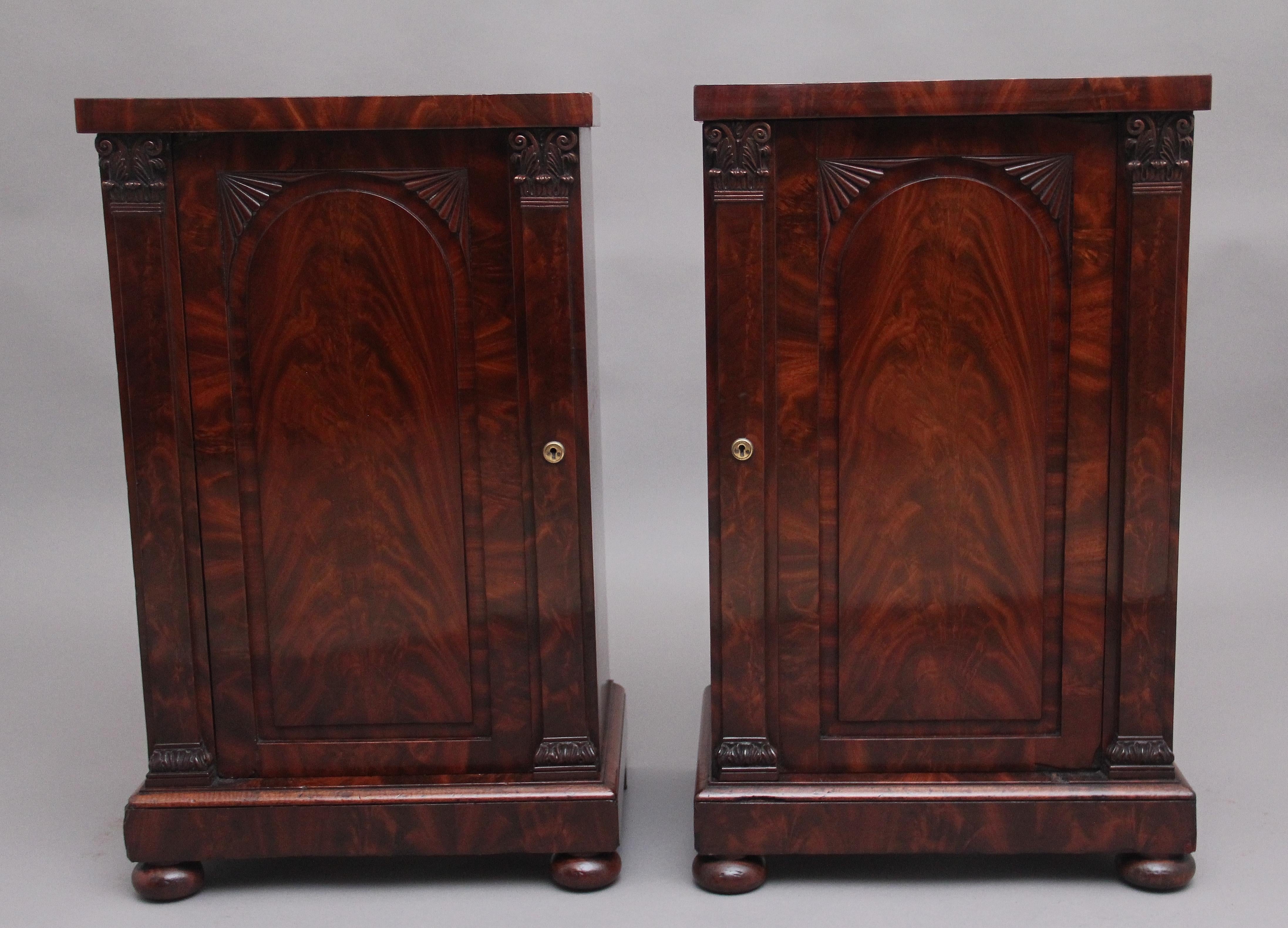 A pair of 19th Century flame mahogany bedside cabinets, nice figured top above a cupboard door opening to reveal a single fixed shelf inside, the door fronts having a central oval panel with carved decoration at the top, columns at either side with