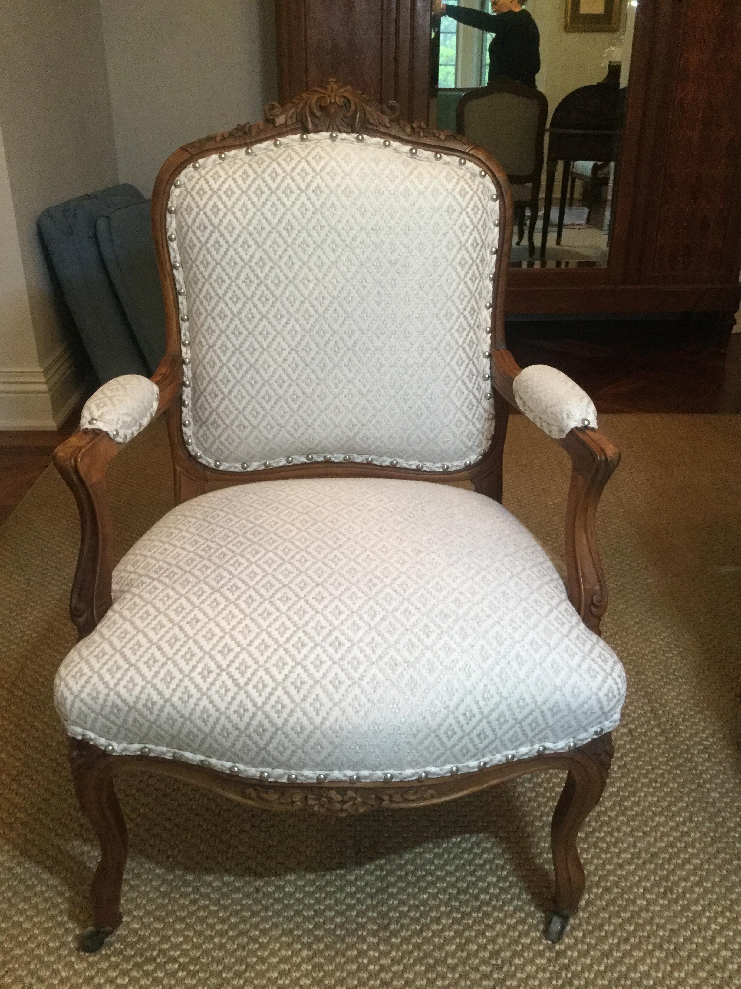 Stunning pair of later 19th century French armchairs. Made of walnut, these chairs feature a beautifully carved frame with floral motifs at the crest and on the legs. The designer upholstery is a white on white diamond pattern. There are silver