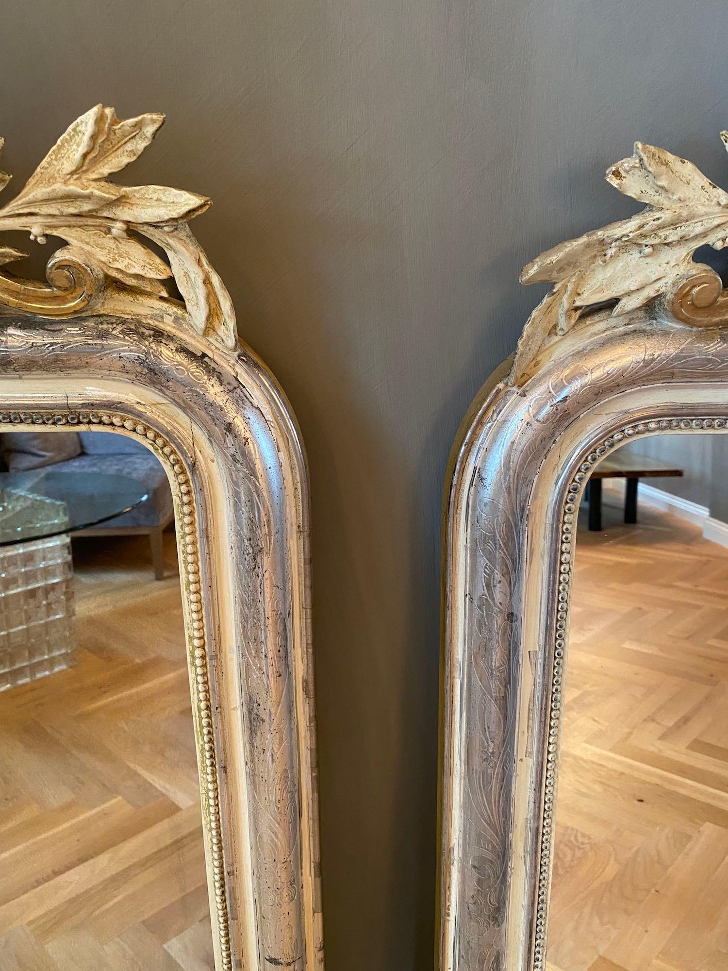 A very unique, decorative and beautiful pair of antique French mirror with its original glass and silver leaf gilding.
The beautiful crown is festooned with carved foliate motifs, scrolls, floral decoration and a small mirror.
The frame is etched