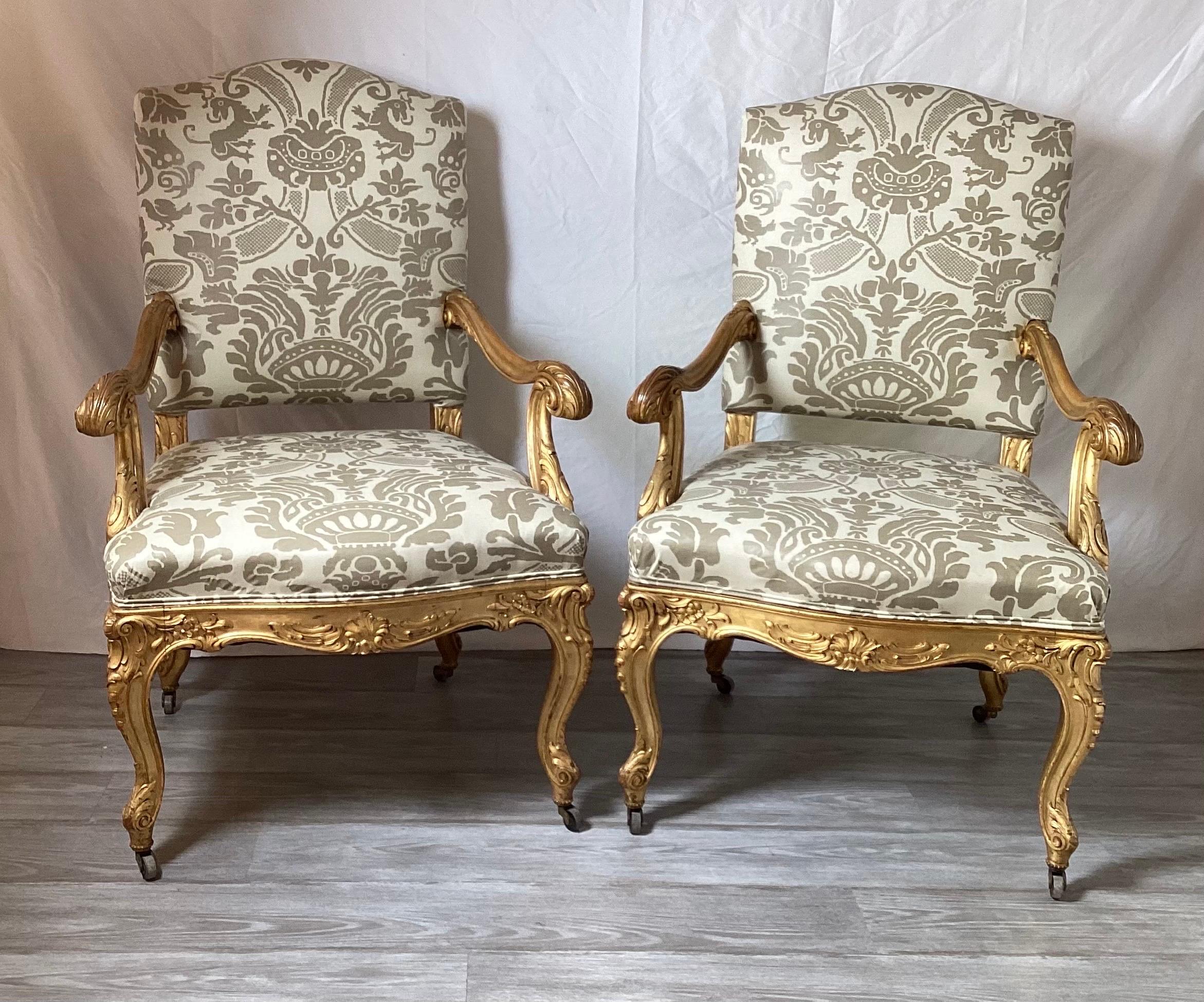 A beautiful pair of hand carved walnut open arm chairs in Newly upholstered vintage Fonisetti style large print damask. fabric. The masterfully carved frames with real gold leaf with original age wear on the arms. The chairs newly recovered in a
