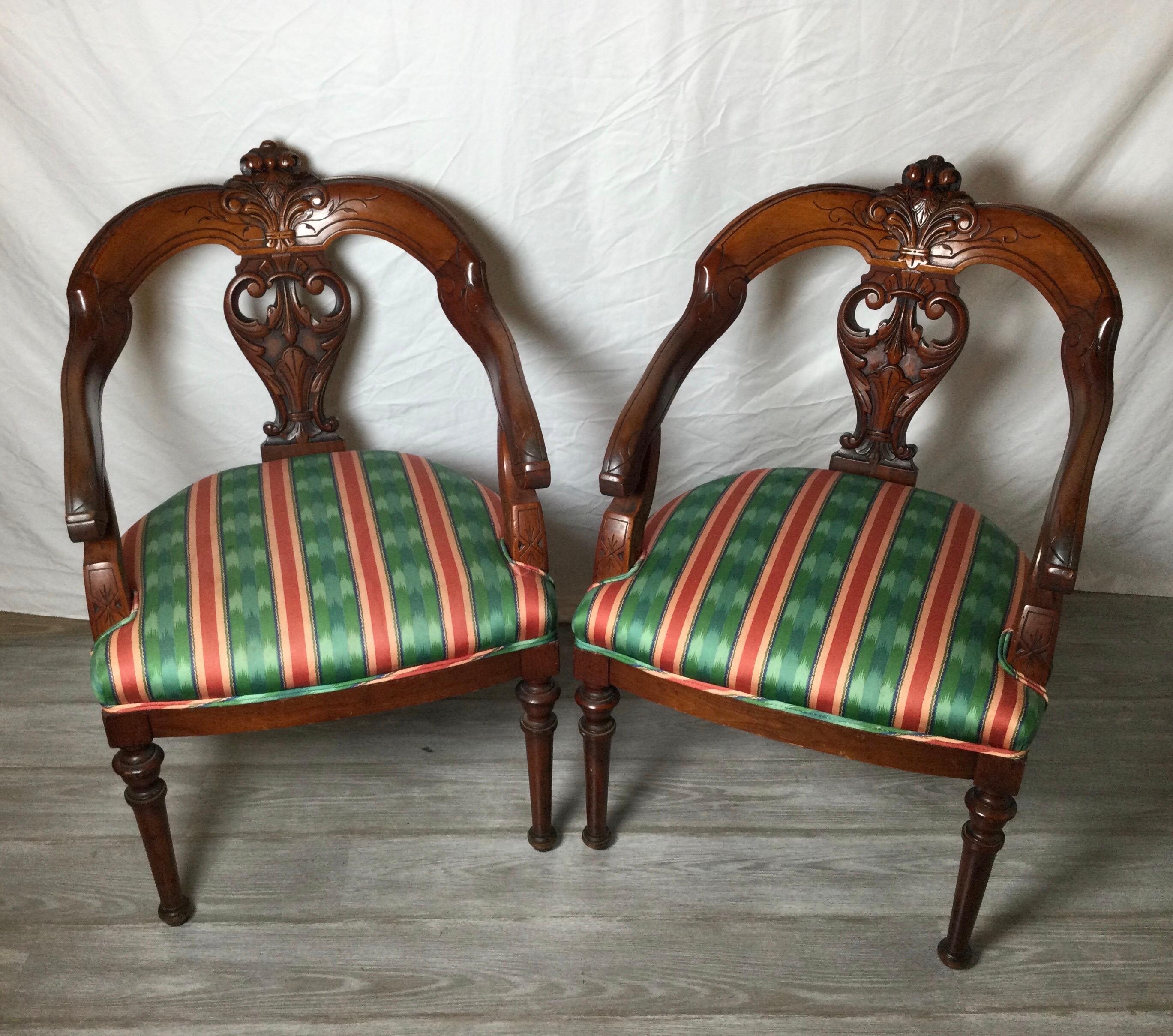 A pair of hand carved walnut rounded back armchairs with new upholstered seat. The chairs with a warm age patination to the wood with hand carved backs.