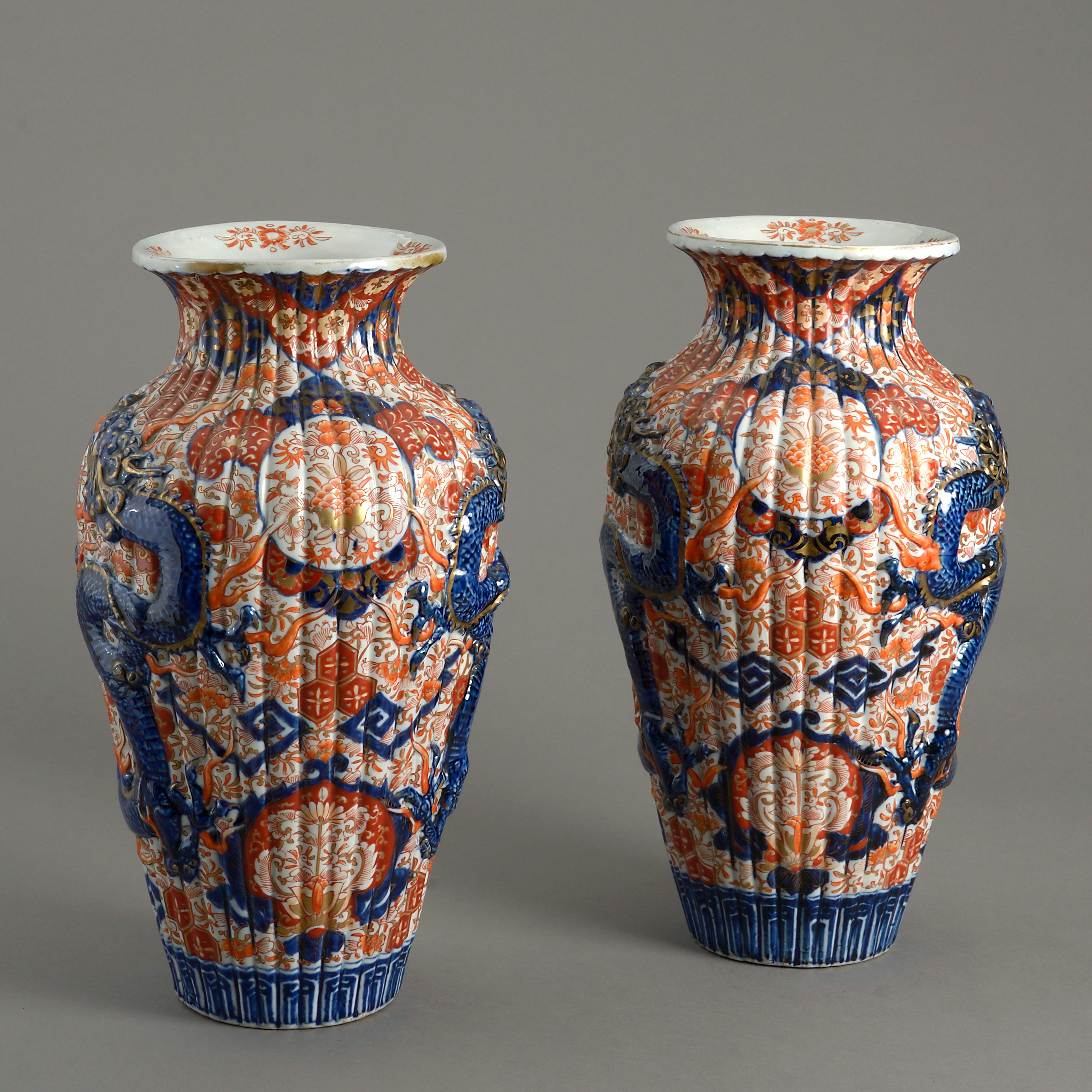 A fine pair of 19th century Imari porcelain vases, the bodies of ribbed form and with blue glazed dragons, modelled in relief, upon an intricately decorated ground in the traditional manner with red, blue and gilt glazes.
  