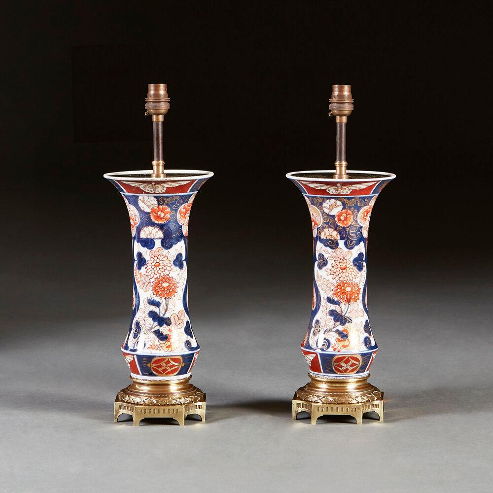 A pair of mid nineteenth century Imari vases, decorated with flowers and butterflies, mounted with French late nineteenth century chased brass bases, now converted as lamps.