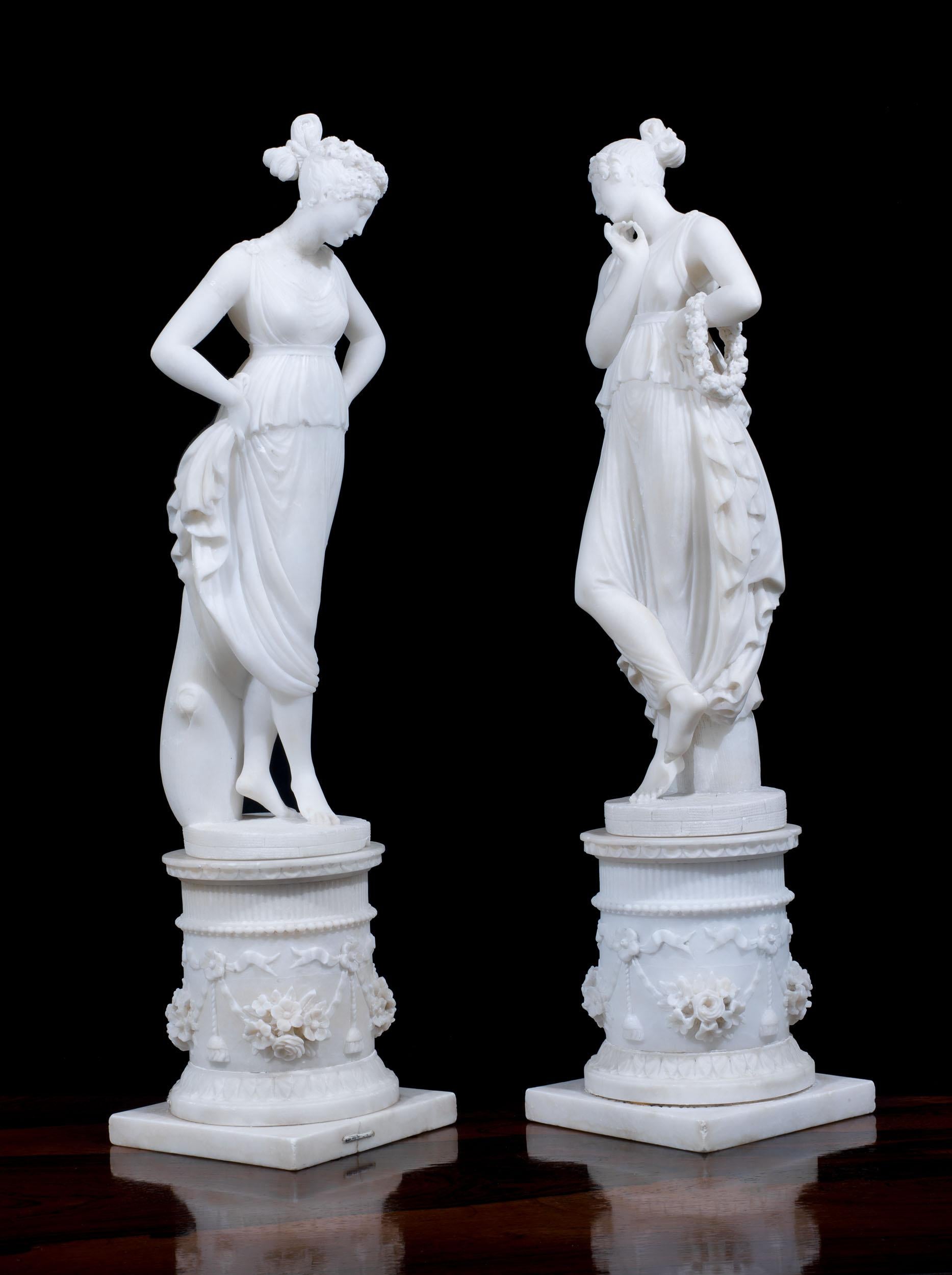 A pair of very finely carved 19th century alabaster figures of muses, in classical dress, each standing on circular pedestals intricately carved with flowers and beading, Italian, c.1850.