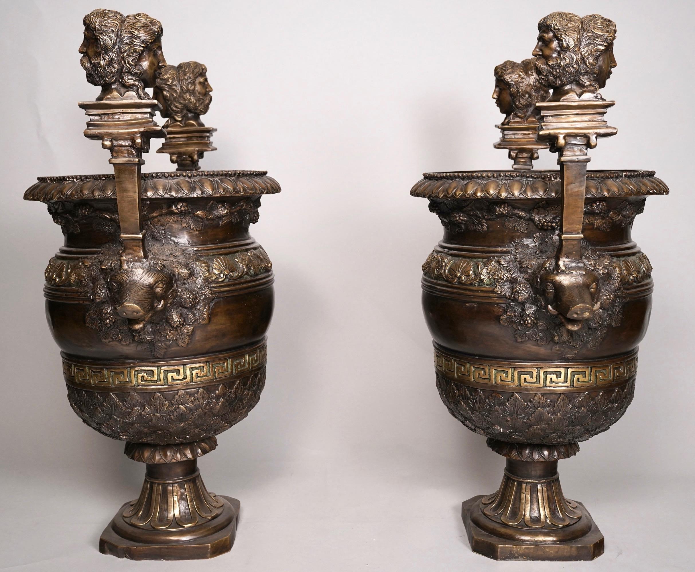 Coppia di urne neoclassiche in bronzo patinato del 1850 circa. Queste bellissime urne hanno manici a testa di cinghiale sormontati da busti di maschere classiche maschili e femminili bifronti, fusi con chiavi greche e decorazioni a fogliame. I