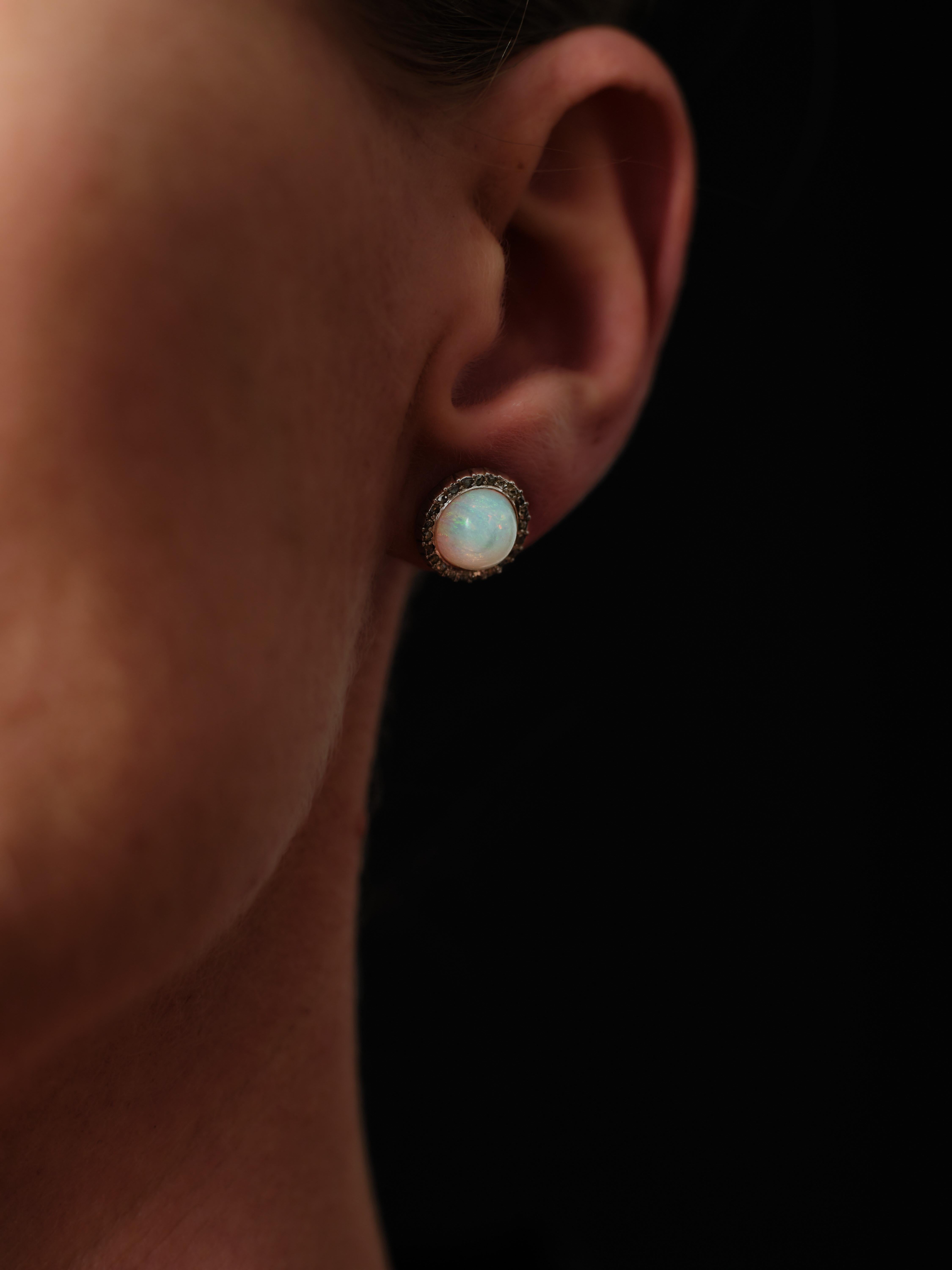A pair of pastel-colored, round cabochon opals are flanked by shimmering rose-cut diamonds, set in darkened silver over 18kt. gold, in these charming and lively ear poppers. 

The earrings give of that special outer worldly opal radiance that just