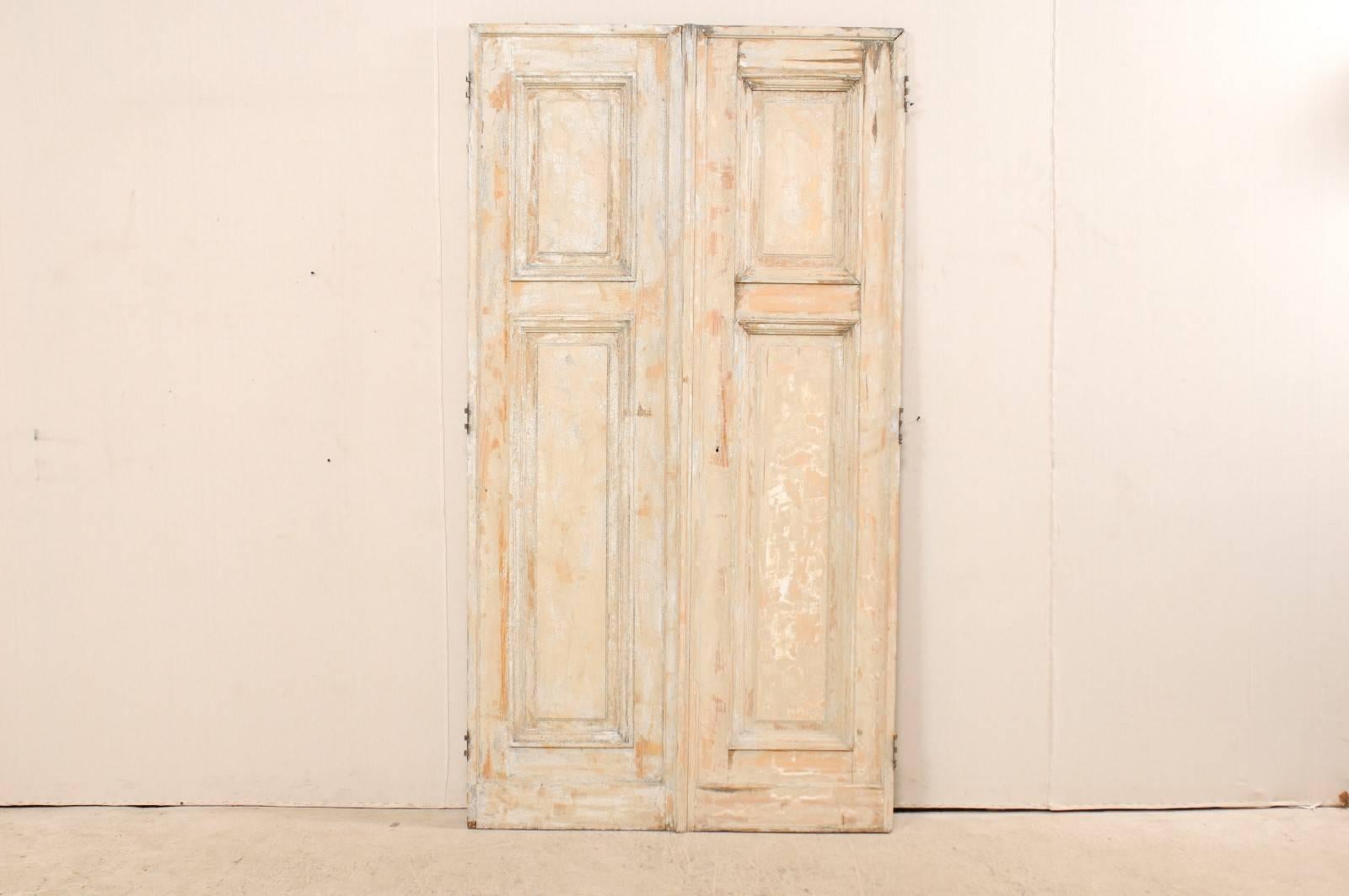A pair of 19th century French doors. This pair of French doors each feature two recessed panels, with a shorter vertical rectangular-shaped panel at the top over a longer lower panel set into their front facing sides. These doors have a scraped