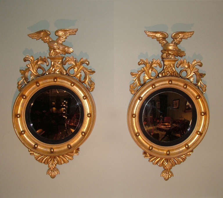 A pair of mid-19th century carved giltwood convex mirrors, with ball decorated moulded frames, having eagle pediments flanked by leaf scroll decoration and pineapple carved finials below.